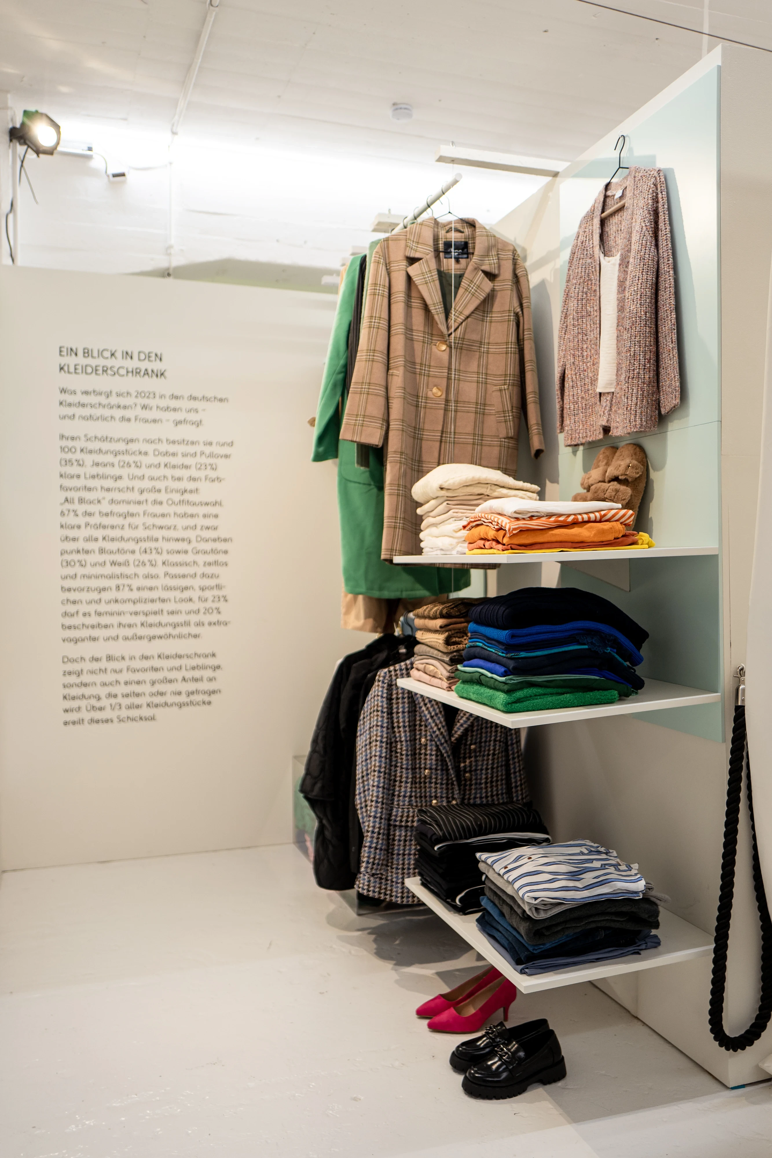 Wardrobe display with jackets, folded knitwear and shoes next to a text panel about German closets.