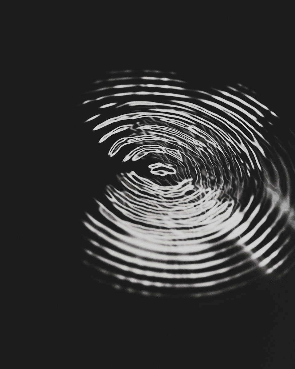 A close-up image of concentric ripples in water, creating a wave pattern against a dark background.