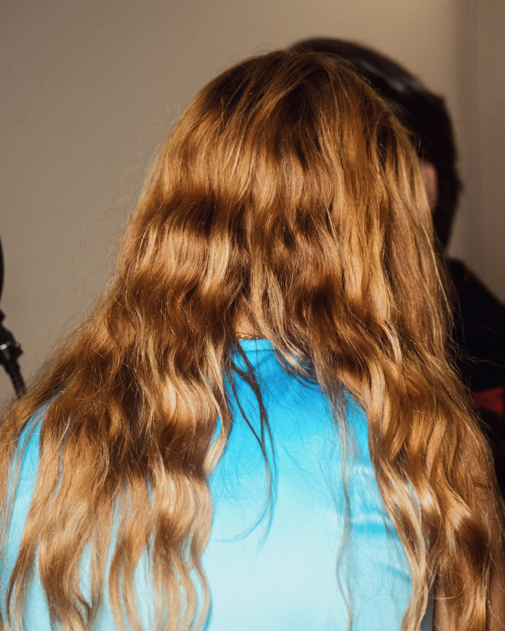 Portrait de dos d'une femme aux longs cheveux bouclés dorés portant un t-shirt bleu