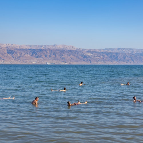 People floating in a calm body of water with a mountain range in the background under a clear blue sky.