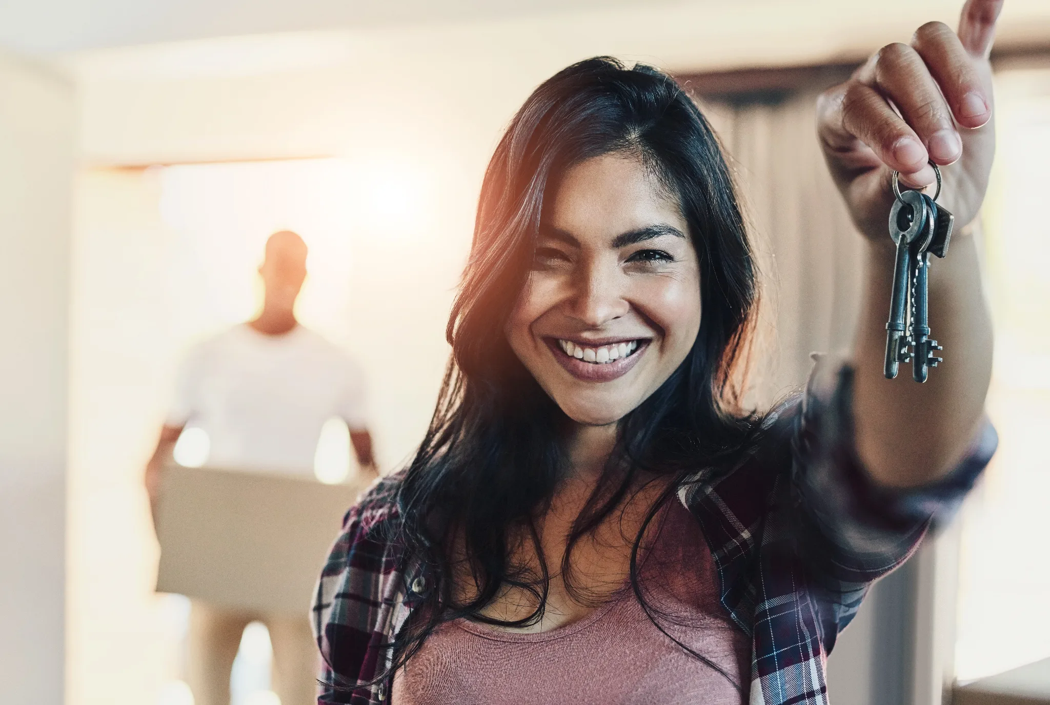 Female smiling with her hands raised in front while holding keys, a man blurred out on the background