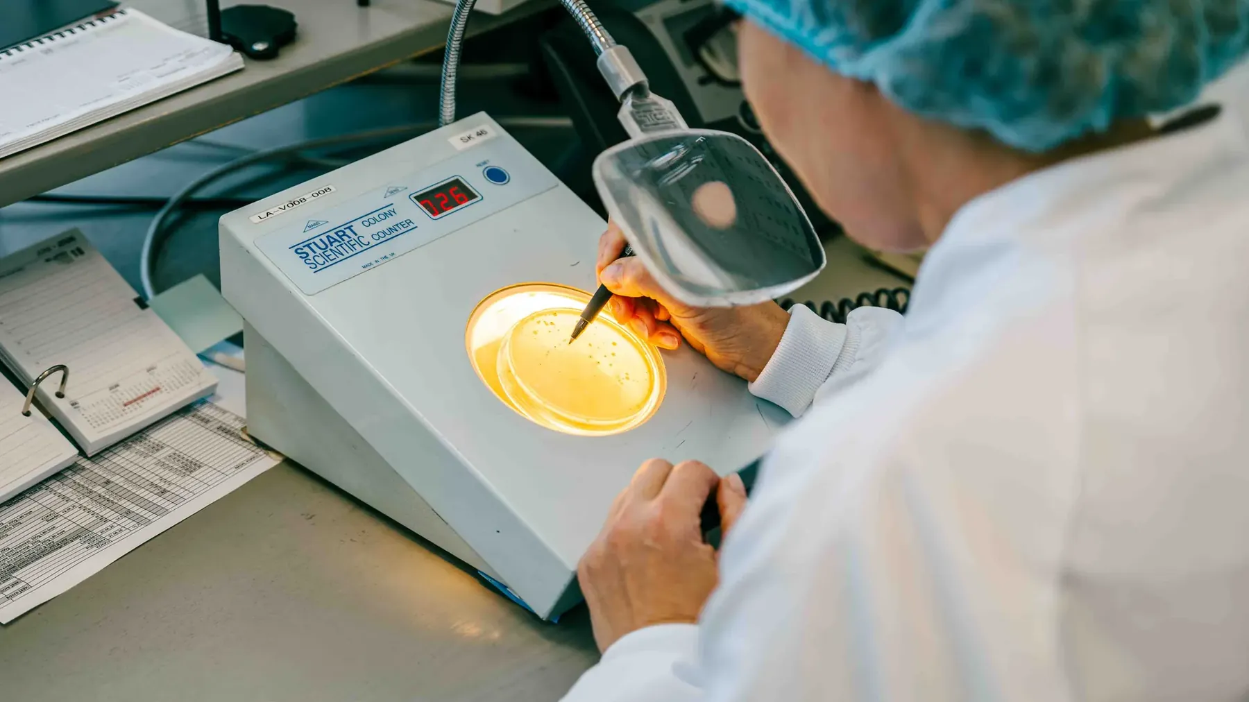Lab technician examining a petri dish using a colony counter