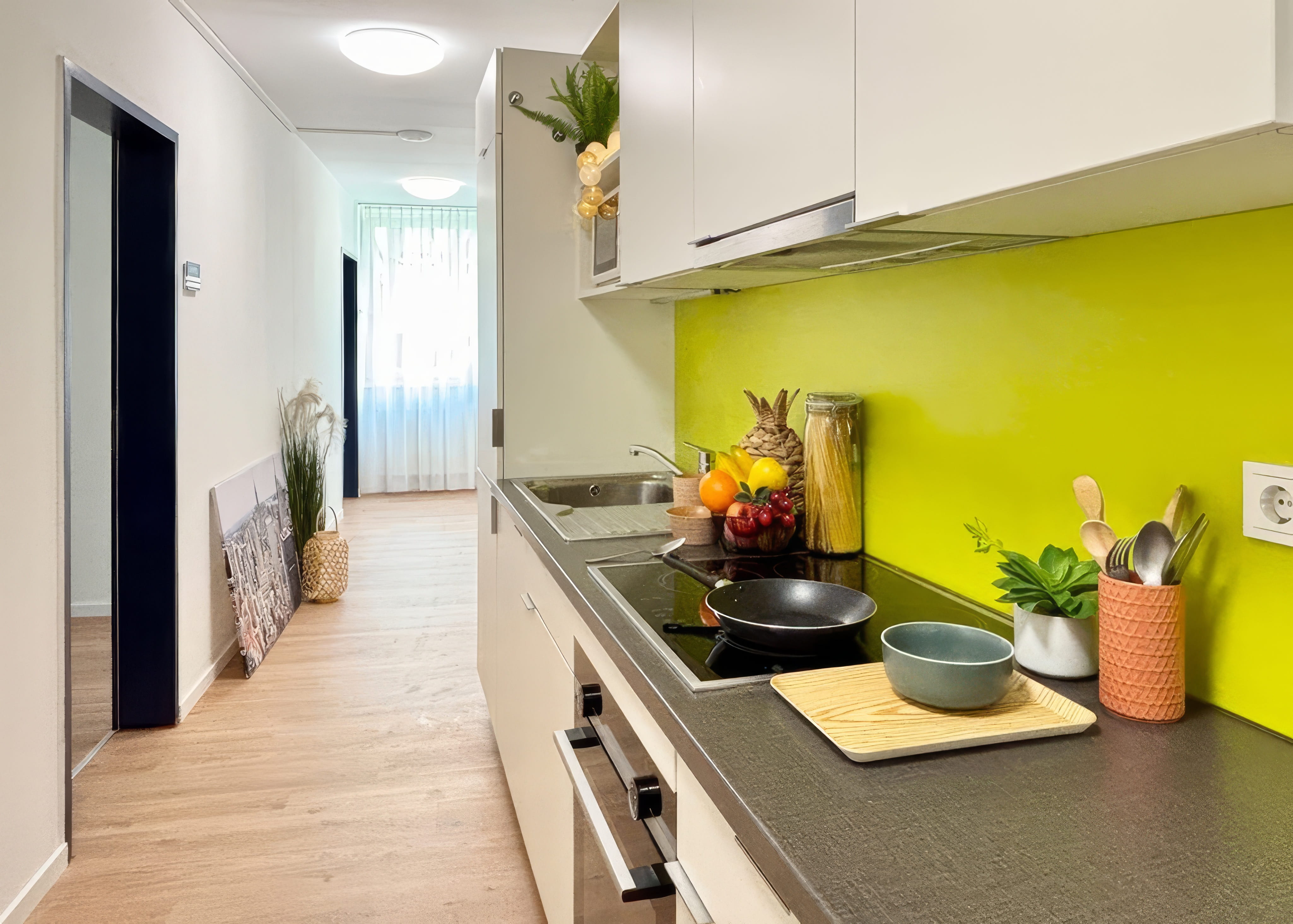 MW Interior - Großzügige Gemeinschaftsküche mit weißen Fronten, grüner Glasrückwand, grünen Polsterbänken und Holzbeistelltischen auf grauem Betonboden" Beschreibung: Einladende Gemeinschaftsküche mit vollausgestatteter Küchenzeile und grünen Lounge-Sitzinseln mit Holztischen – ein Ort, der Kochen, Essen und soziales Miteinander auf einer Fläche vereint und durch konsistente Farbgebung in Grün und Weiß Identität schafft.