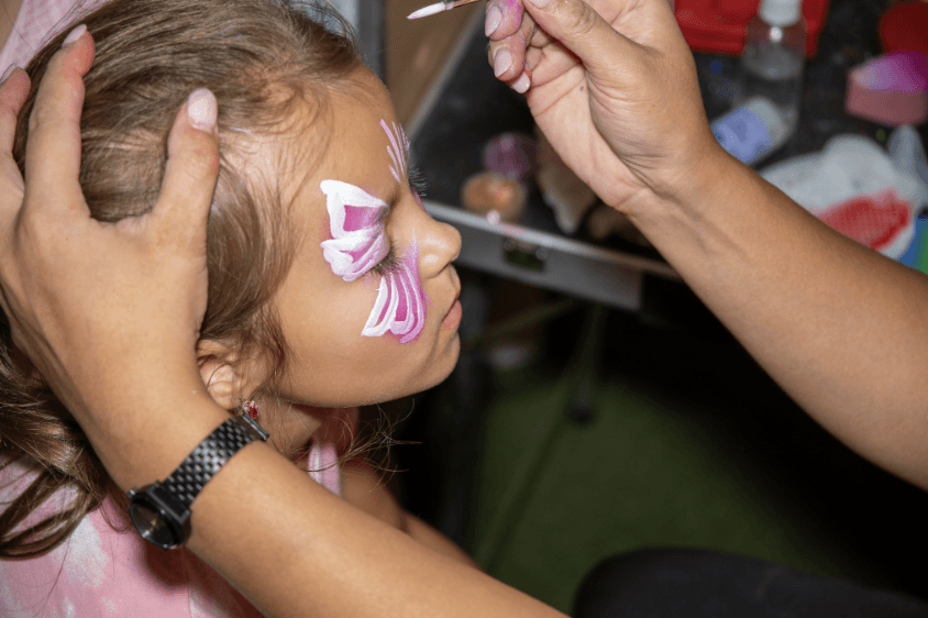 Girl getting a butterfly painted on her face by an artist at a birthday party 