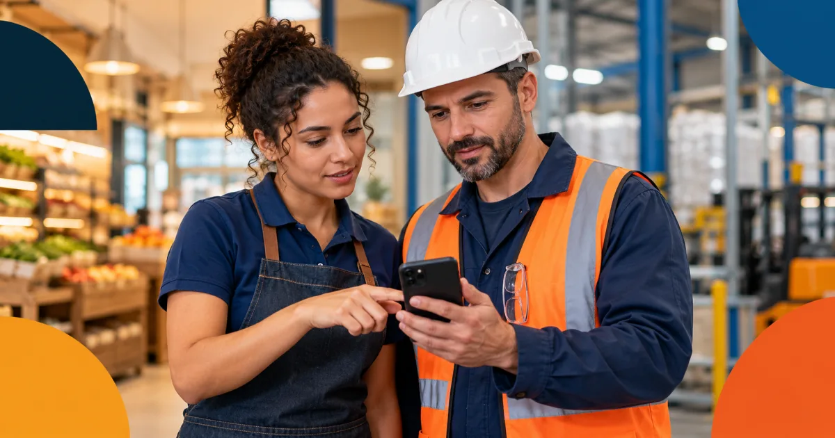 Trabalhadora de loja e profissional de área industrial consultam juntos um celular em um ambiente que combina loja e fábrica.