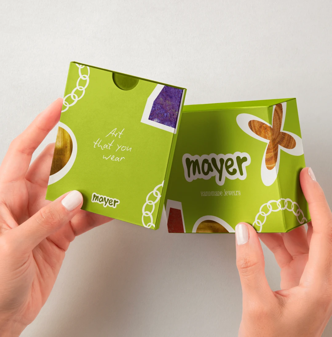Mockup packaging boîte Mayer Handmade Jewelry — fond vert chartreuse avec collages de matières brutes (bois, pierre, minéral), tagline "Art that you wear", design unboxing cohérent avec l'identité de marque, Tartelette Concept