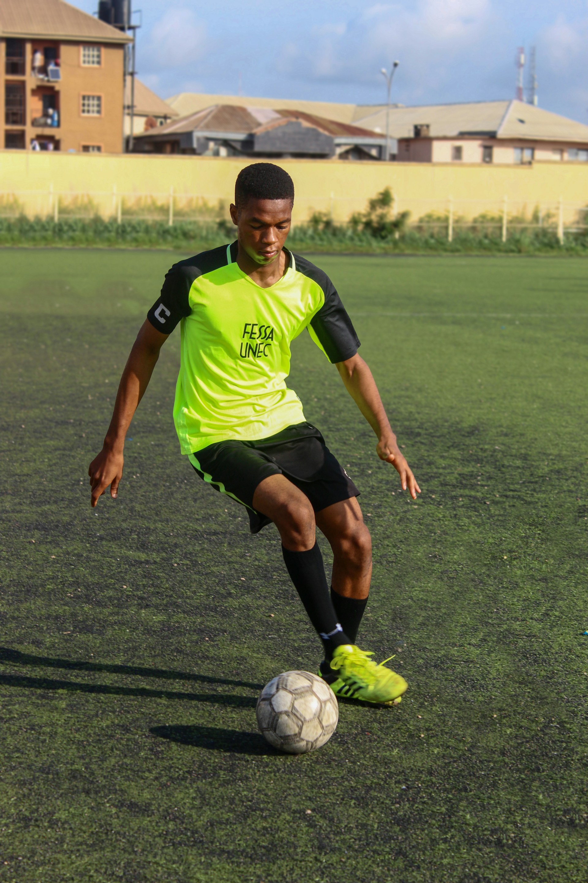 A young male soccer player in a neon green jersey dribbling a ball on an artificial turf field.