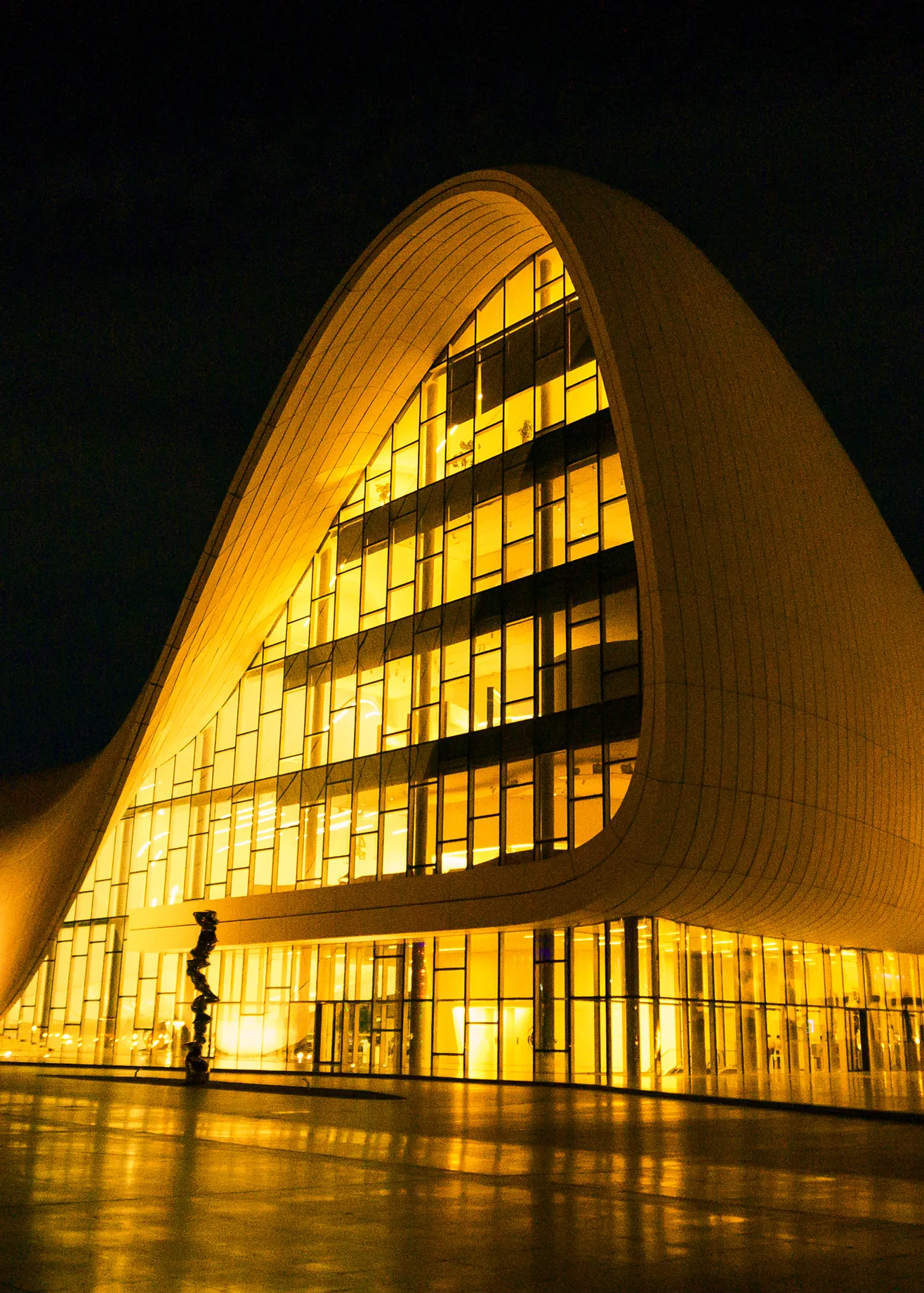 Night view of a distinctive arched golden building with bright interior lights.