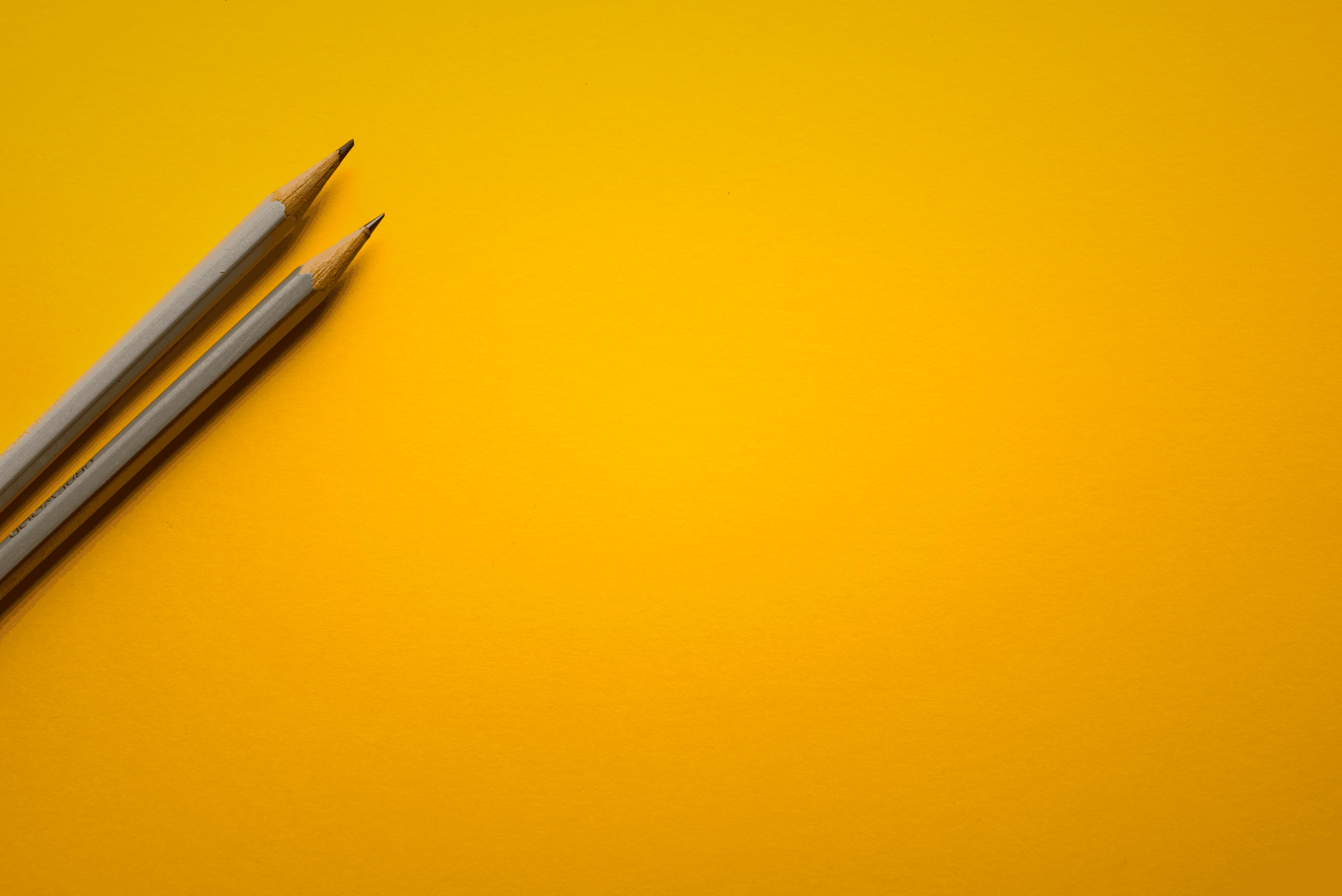 two gray pencils on yellow surface