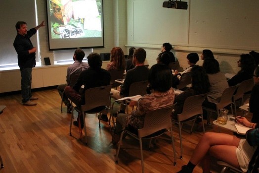one man presenting and explaining based on an image as reference to a room full of people