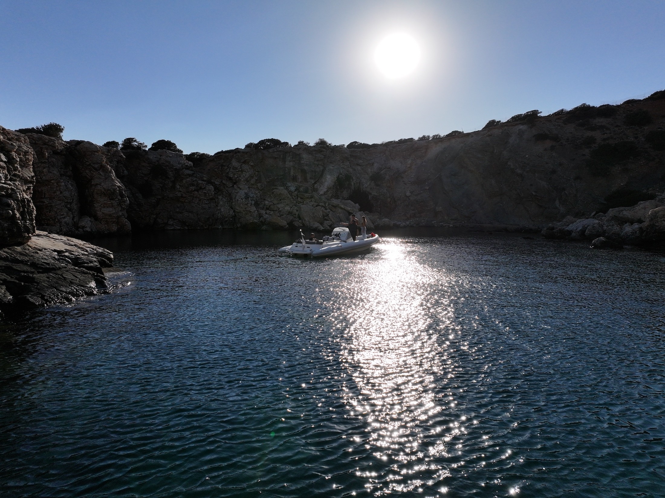 White luxury yacht deck with plush seating anchored in crystal-clear turquoise waters near a rocky Mediterranean coastline.