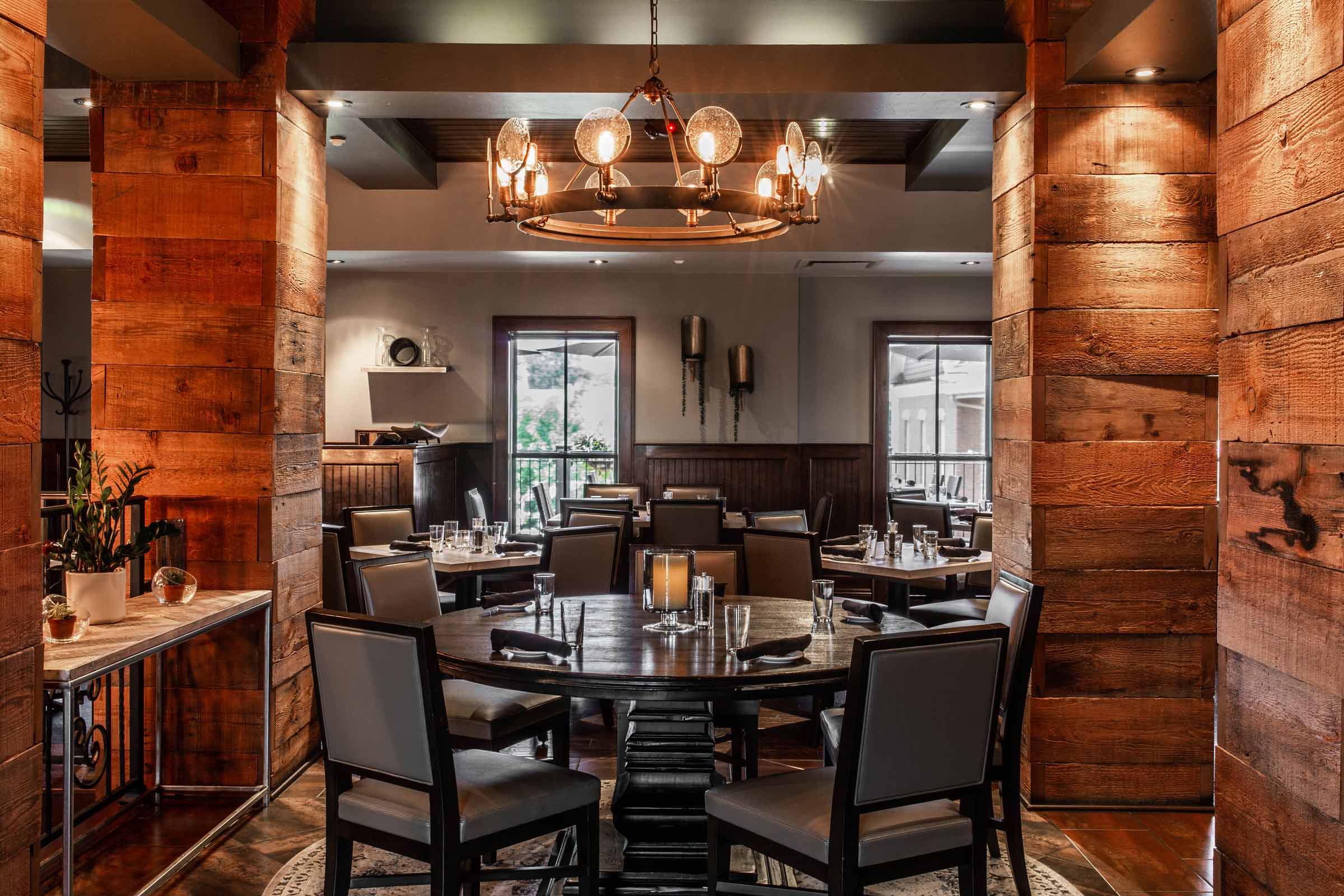 Round table under an iron chandelier framed by reclaimed wood columns at Mezzo