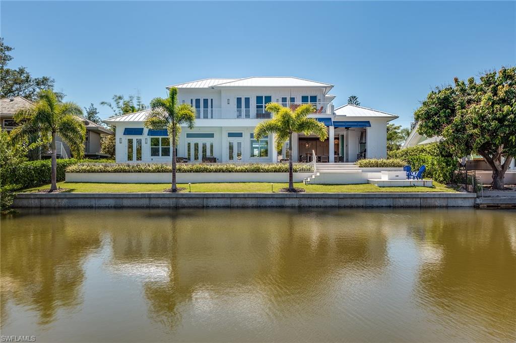 a large white home in the center of the frame with a canal in the foreground lined with palmtrees