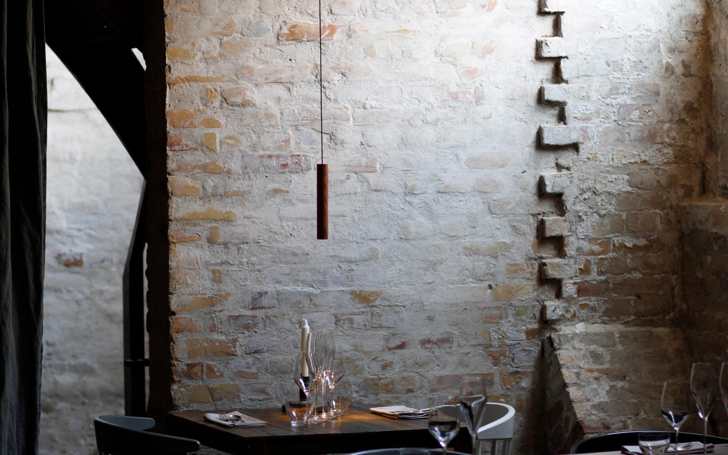 Chimes pendant lamp in solid oak suspended against textured brick wall designed by Asger Risborg Jakobsen