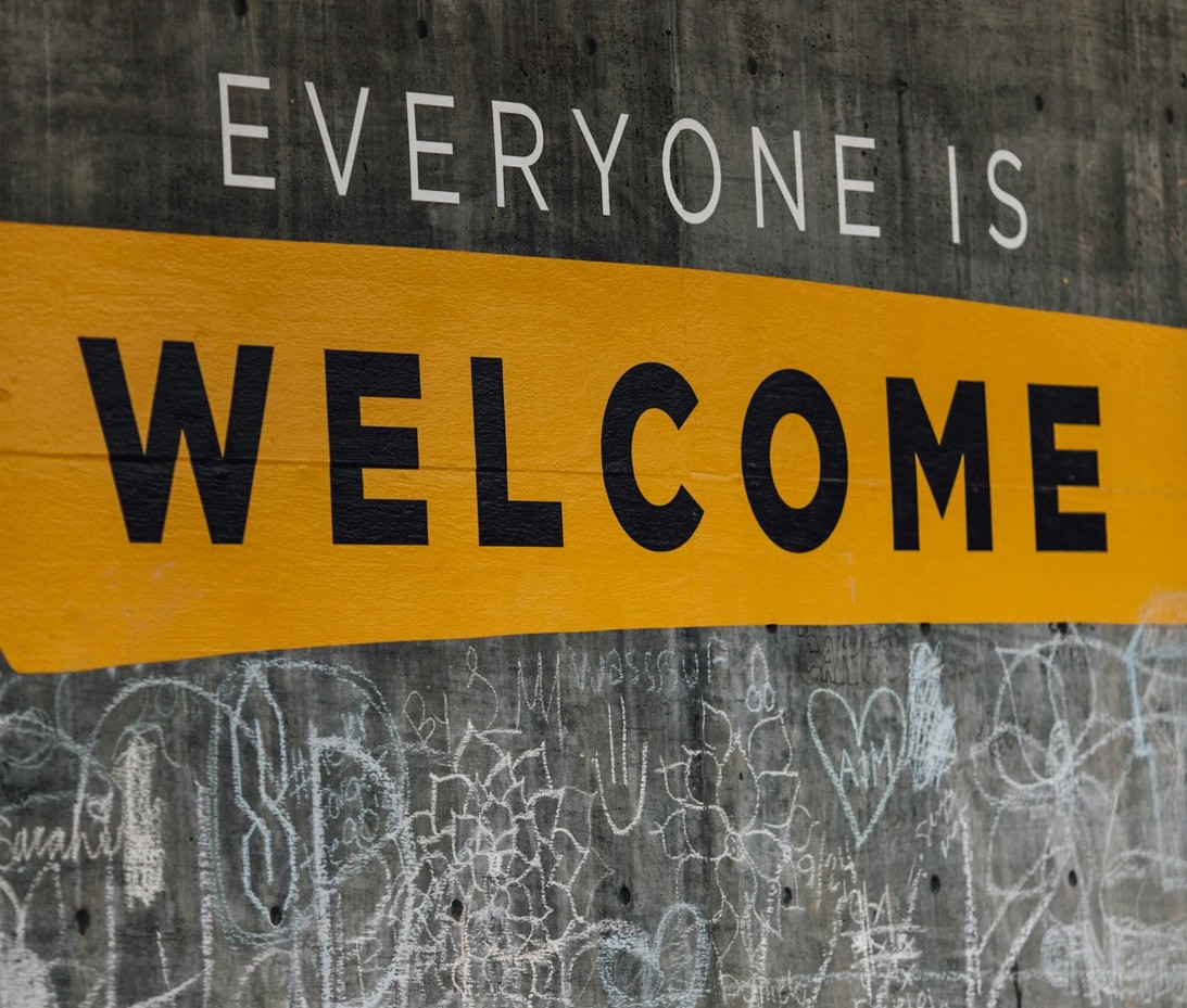 A concrete wall with a bold yellow banner reading 'Everyone is Welcome', with chalk graffiti below.