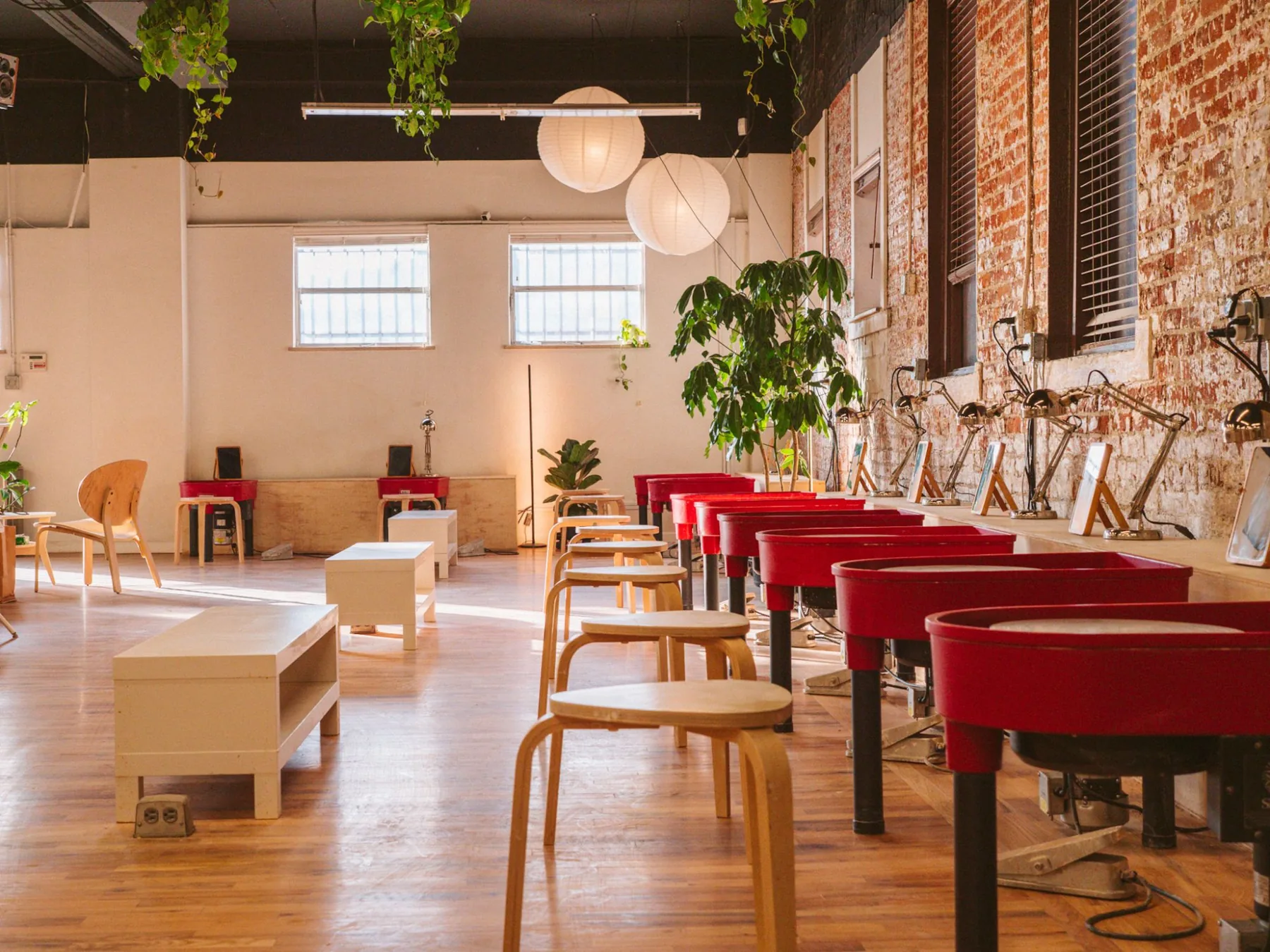 Sunlit row of red pottery wheels under paper lanterns at Kinship, a members-only pottery studio in Denver