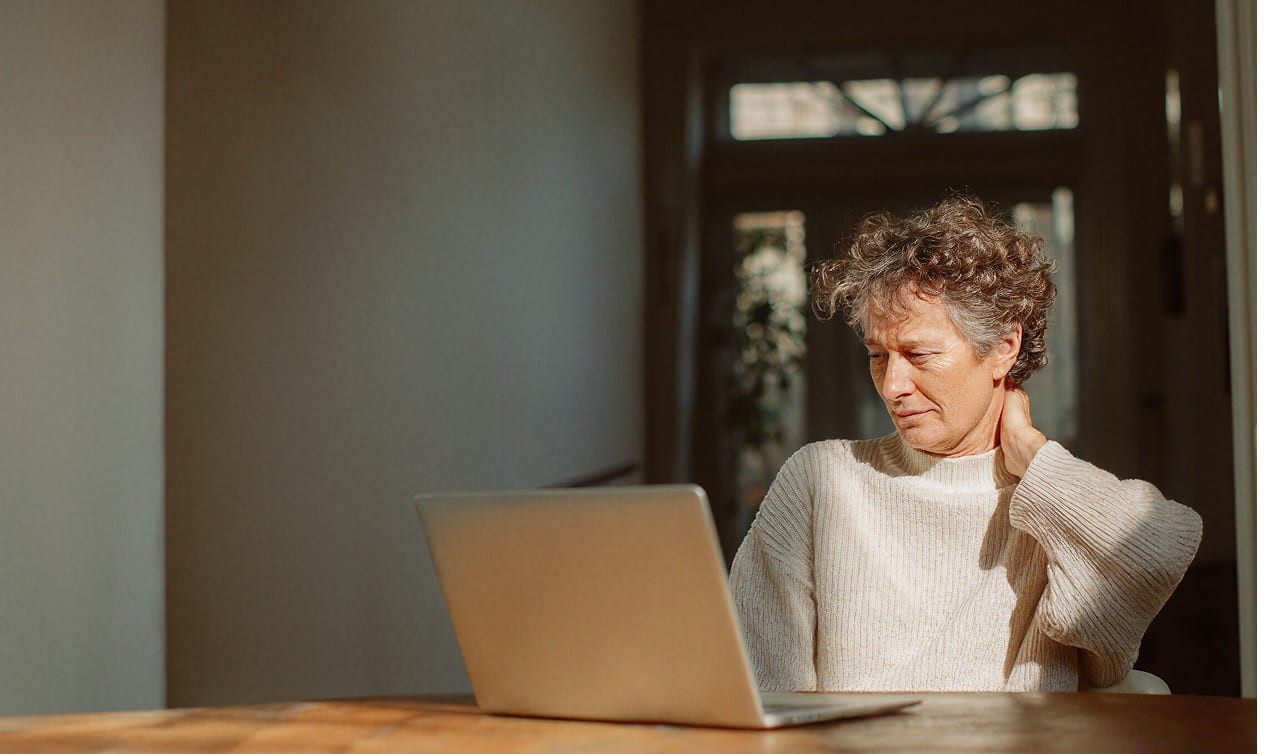 A mid aged men holding his neck in pain while having a video session on his laptop