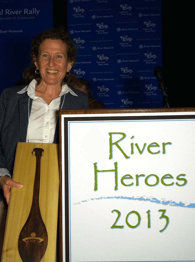 Laura holding a mounted oar next to a sign that says River Heroes 2013