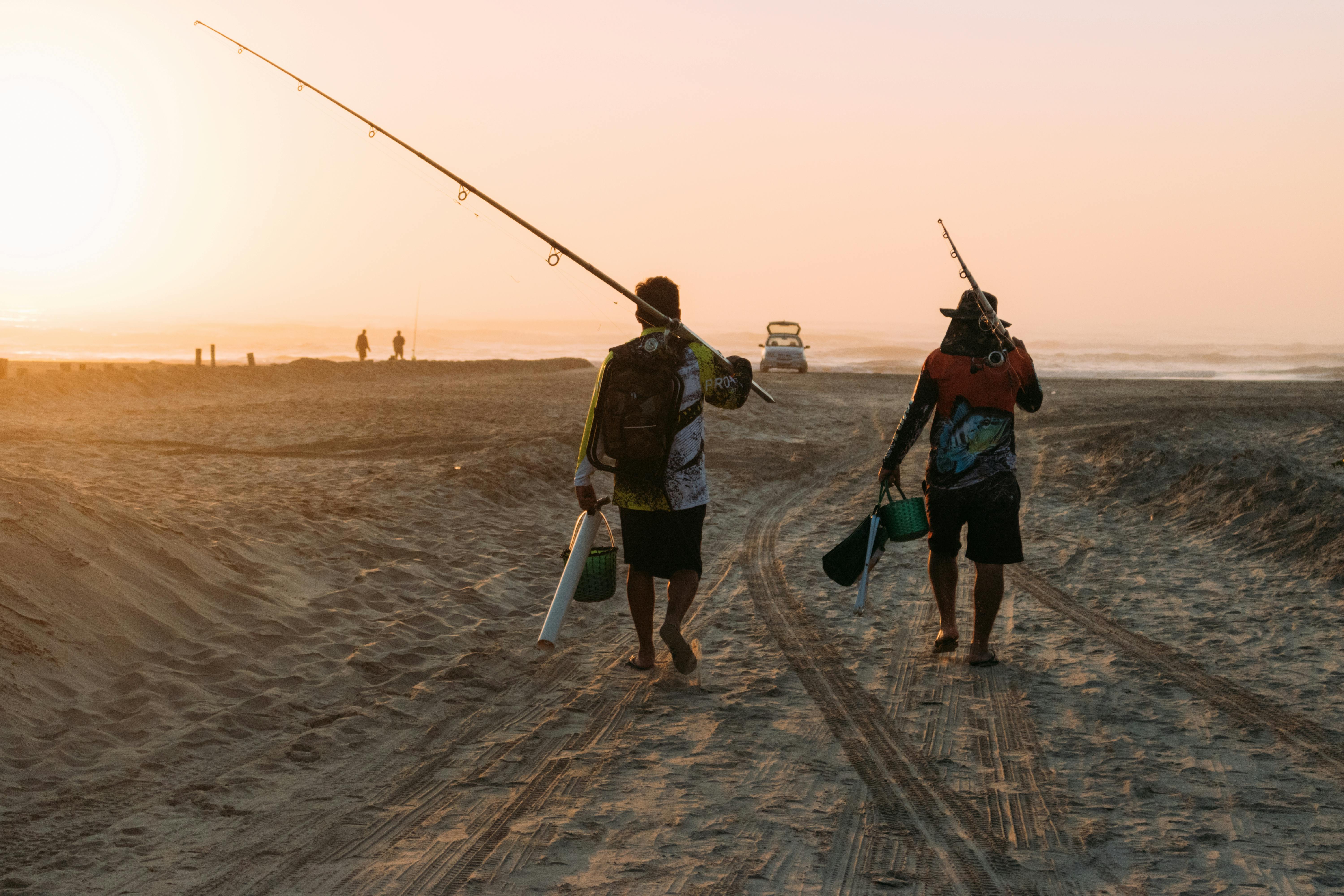 Two figures walking on a sandy landscape at sunset, holding fishing rods, with warm light illuminating the scene.
