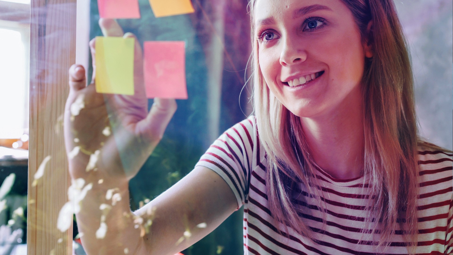 A single woman placing sticky notes on a glass wall