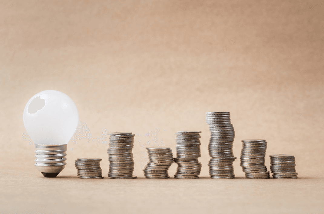 Light bulb placed beside stacked coins of varying heights, representing financial oversight in facilities management