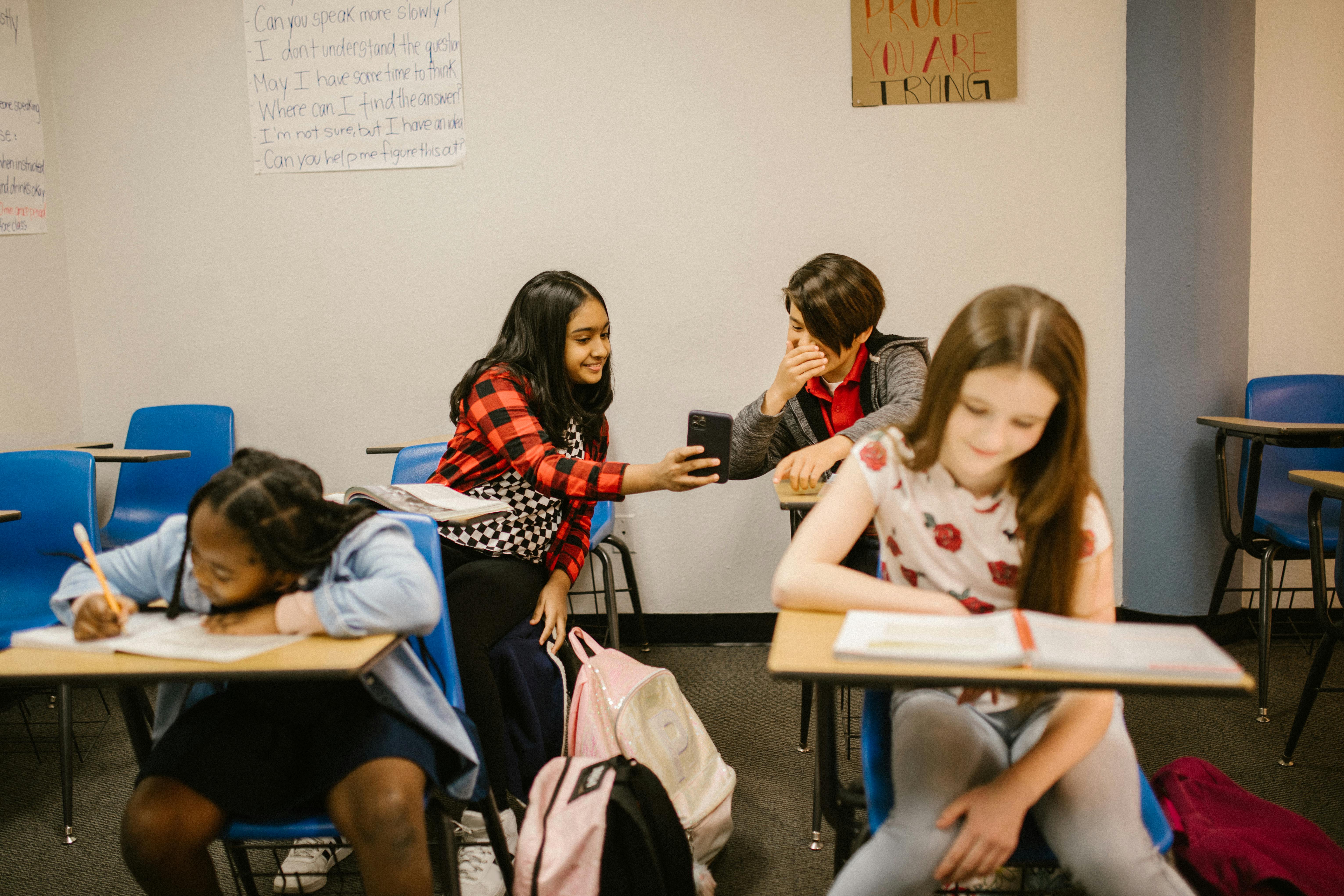 A girl shows a boy a photo on her phone during class.