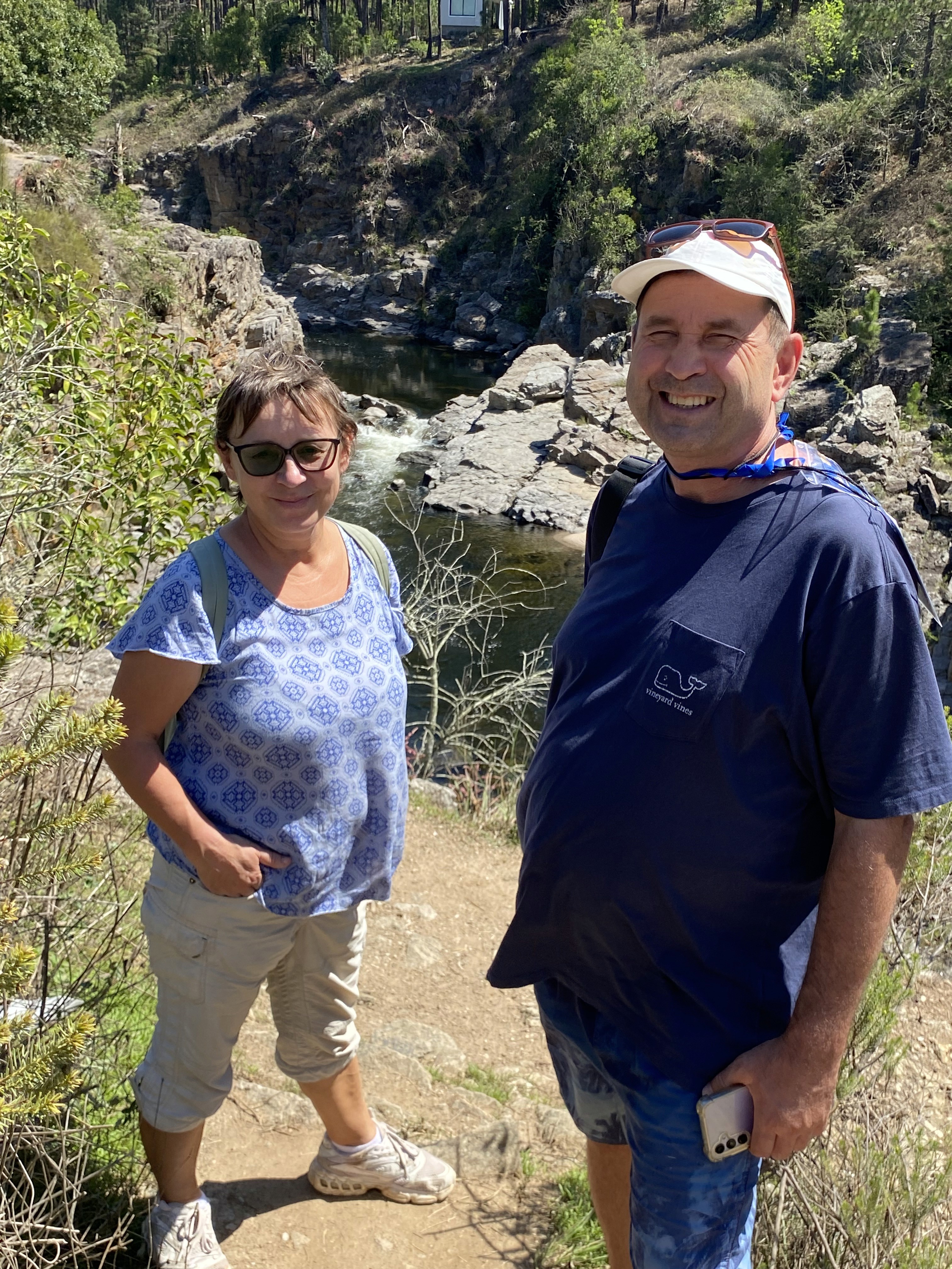 Mujer sentada sobre un tronco frente a una cascada doble en un bosque frondoso de Argentina.