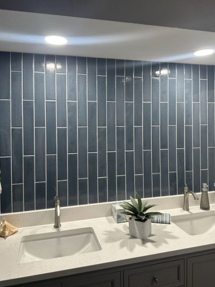 Contemporary bathroom with a blue subway tile backsplash, white double sink vanity, potted plant, and recessed lighting.