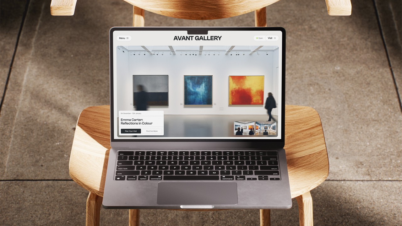 Overhead view of a laptop on a wooden chair, its screen displaying the Avant Gallery website homepage with artwork images and the header “AVANT GALLERY”.
