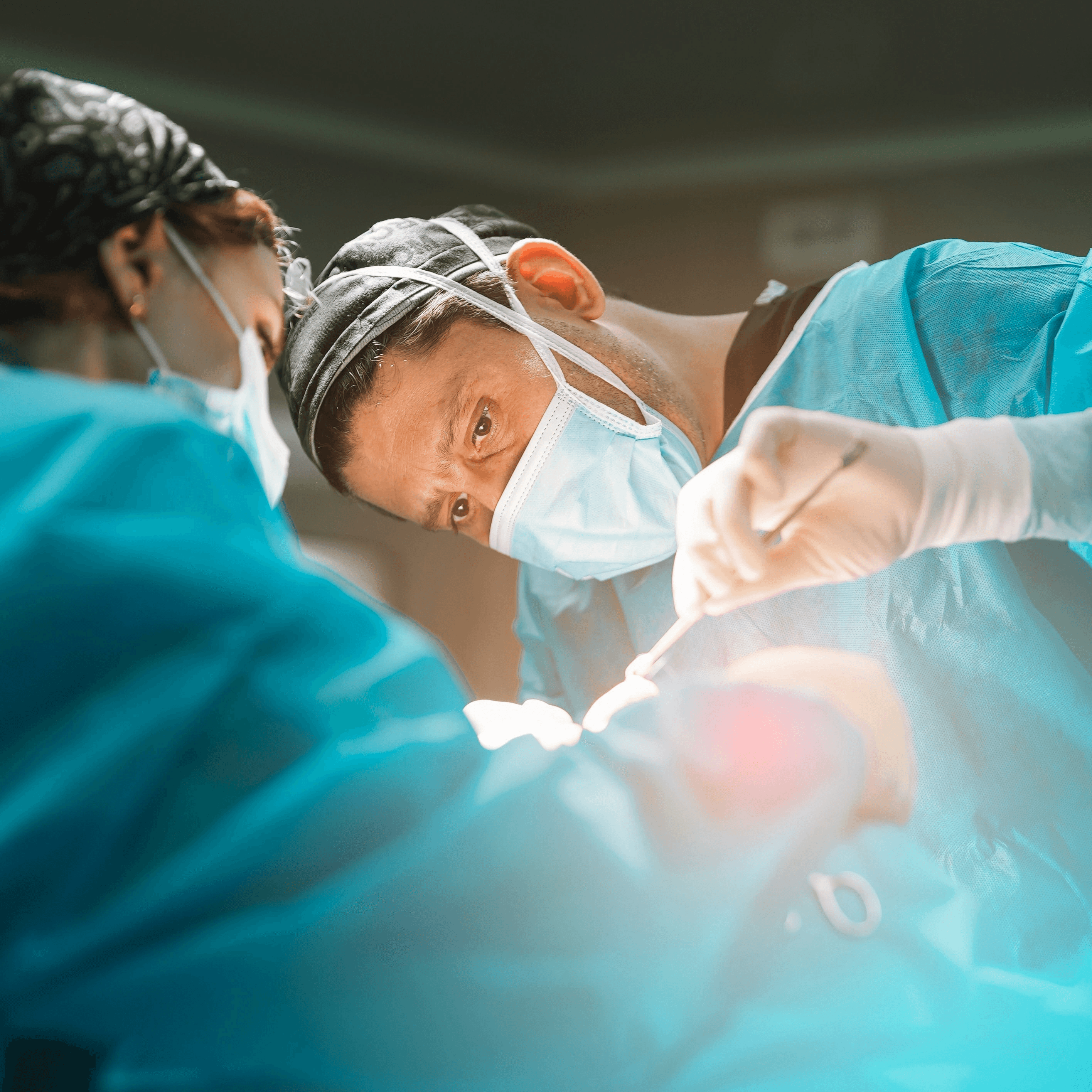 An anesthesia provider in surgical scrubs and gloves cares for a patient under operating room lights