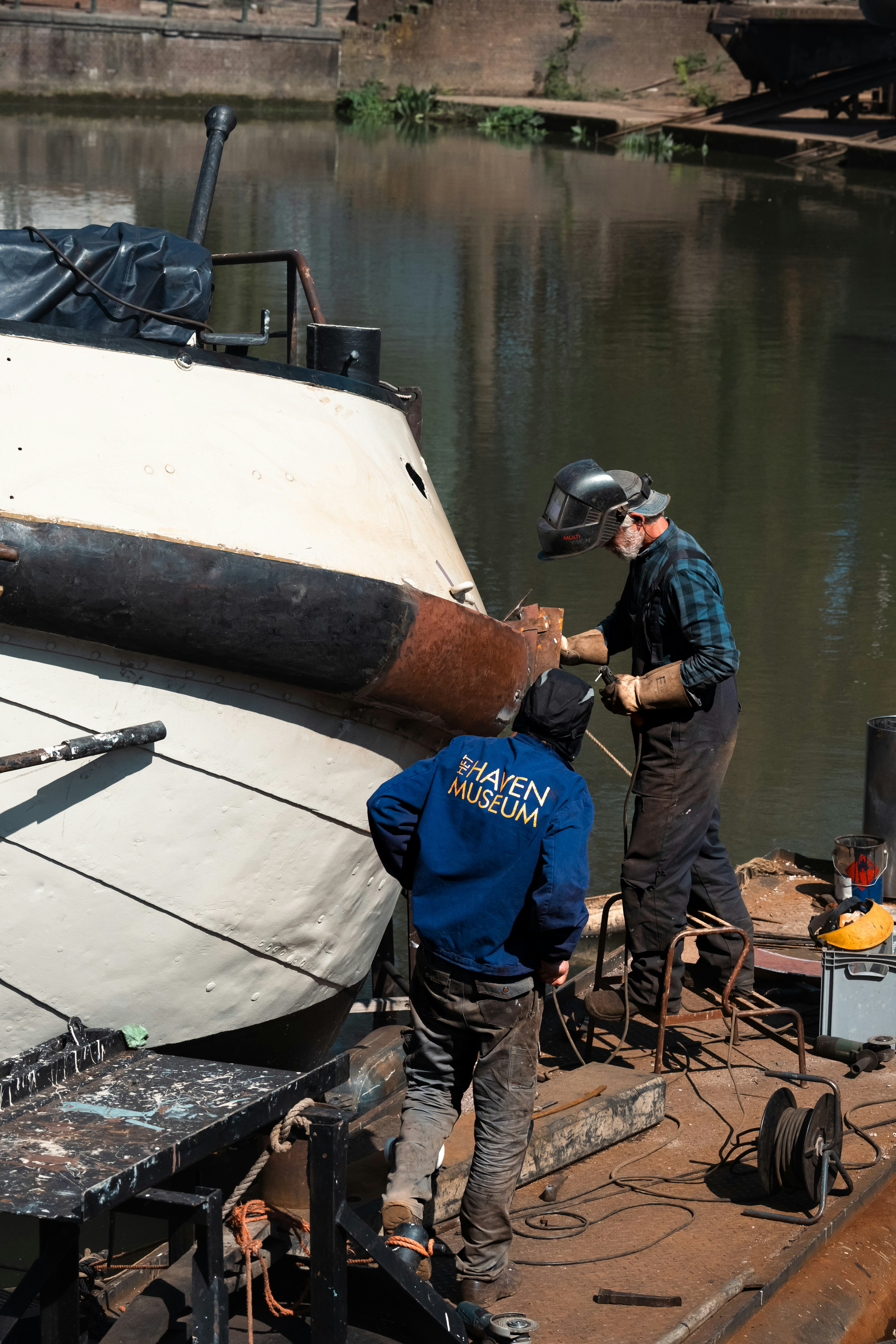 Workers are welding on a boat in a canal.