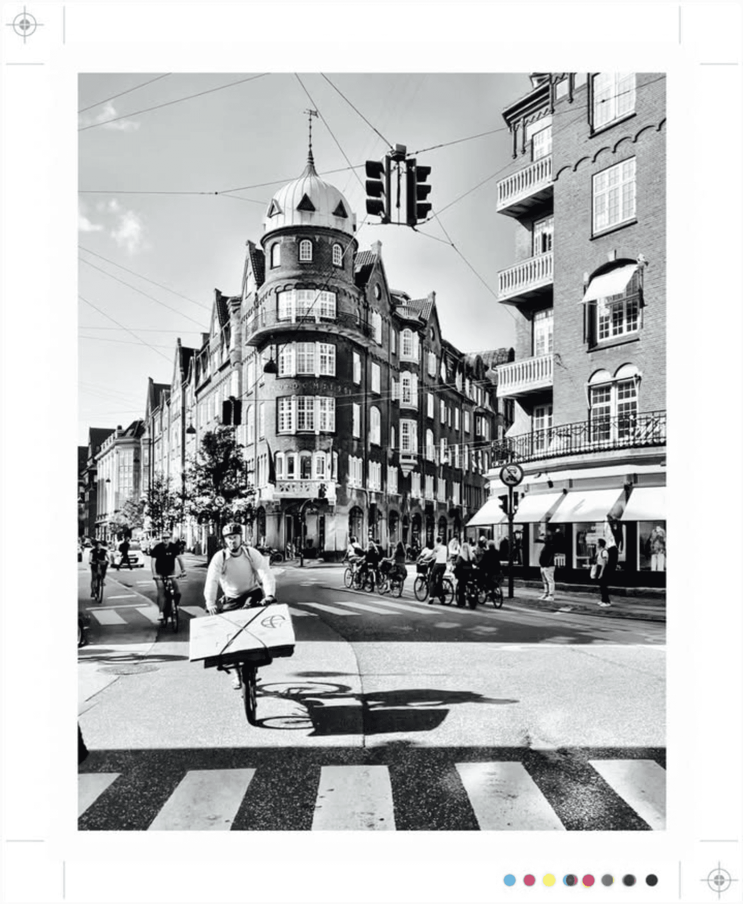 Zwart-wit stadsgezicht met fietsers op een oversteekplaats en gebouwen.