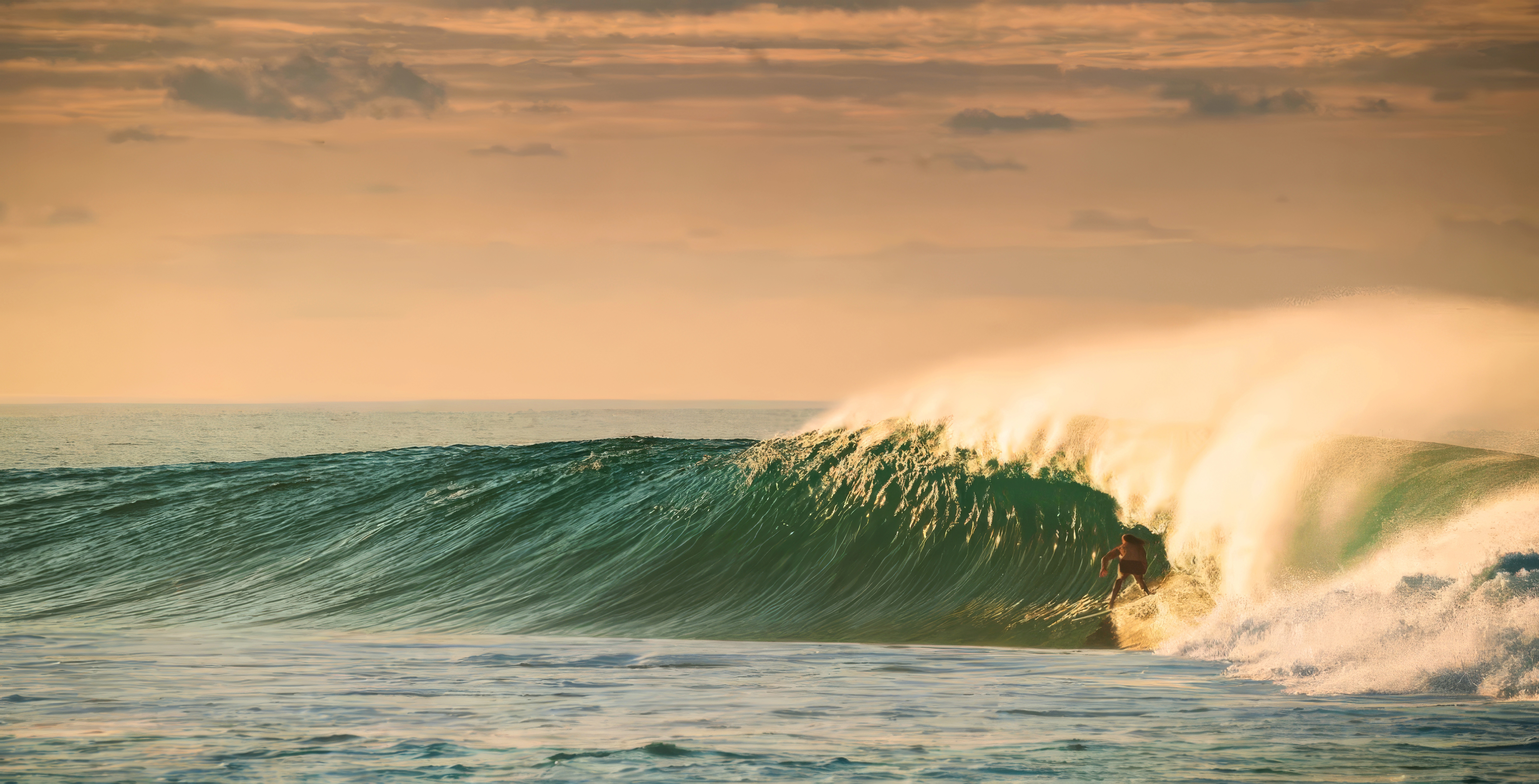 Surfer riding a powerful green wave barrel at sunset with golden sky.