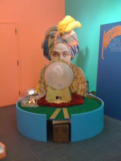 a statue made from hard materials with a face of a person hidden by a crystal globe, and at the base, it has a hole for a mini-golf course