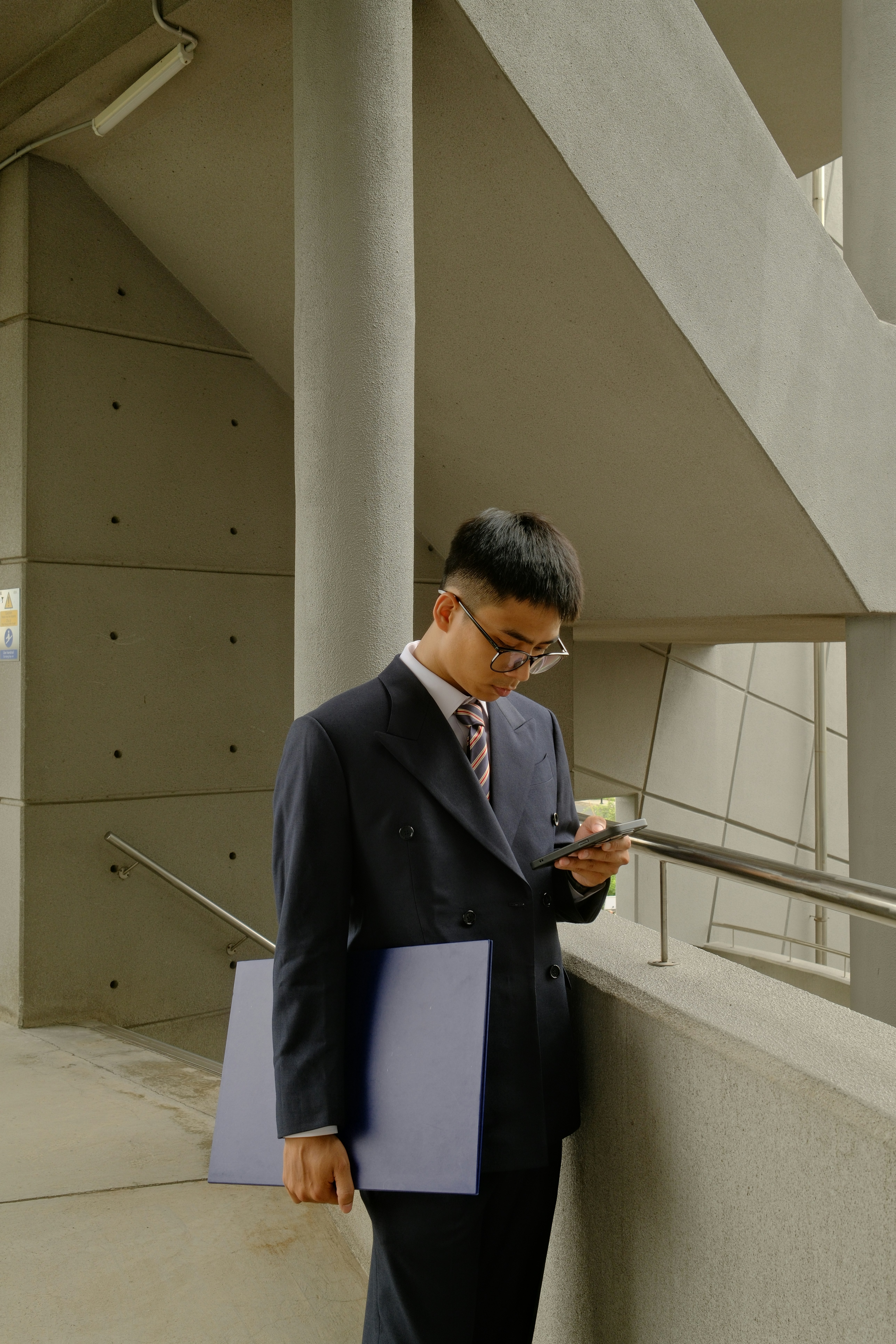 Man in suit checks phone near concrete stairs.