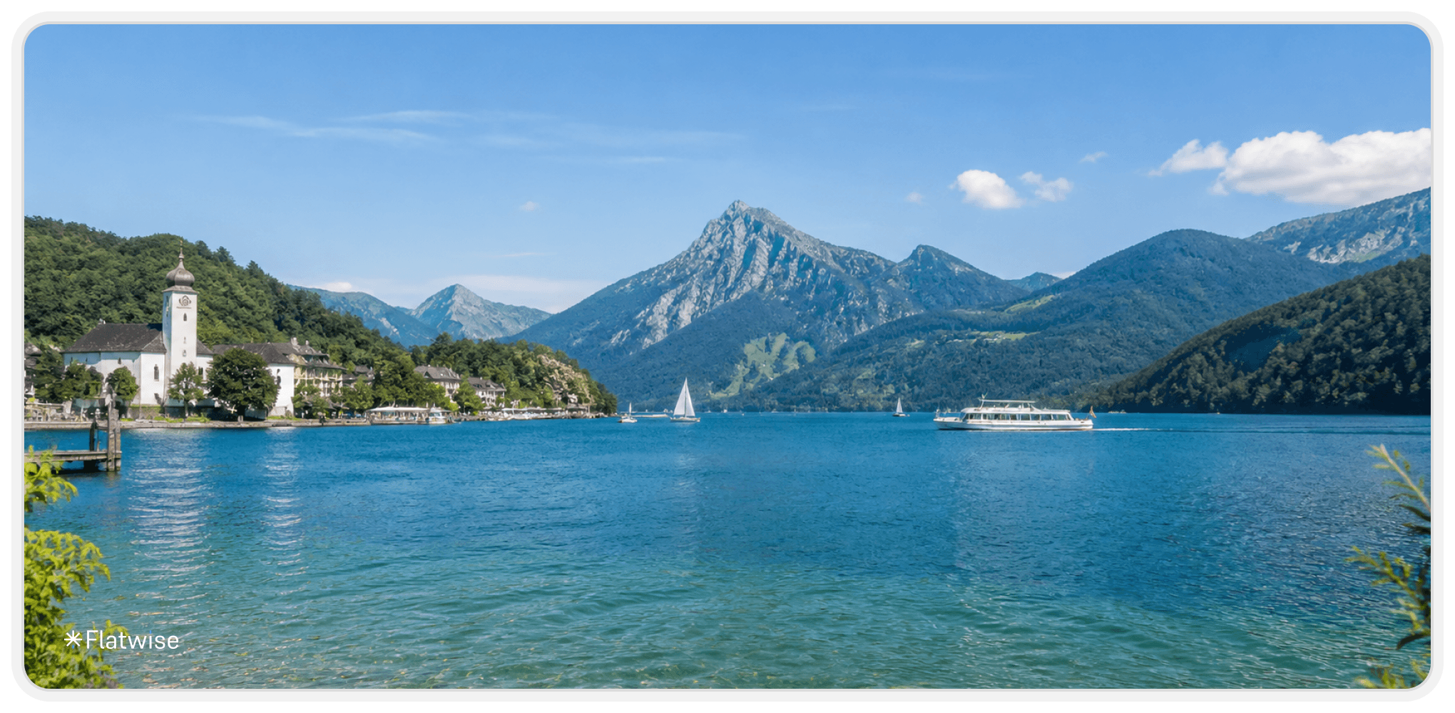 Ein wunderschöner See im Salzkammergut mit türkisem Wasser. Man erkennt eine Kirche und Berge im Hintergrund.