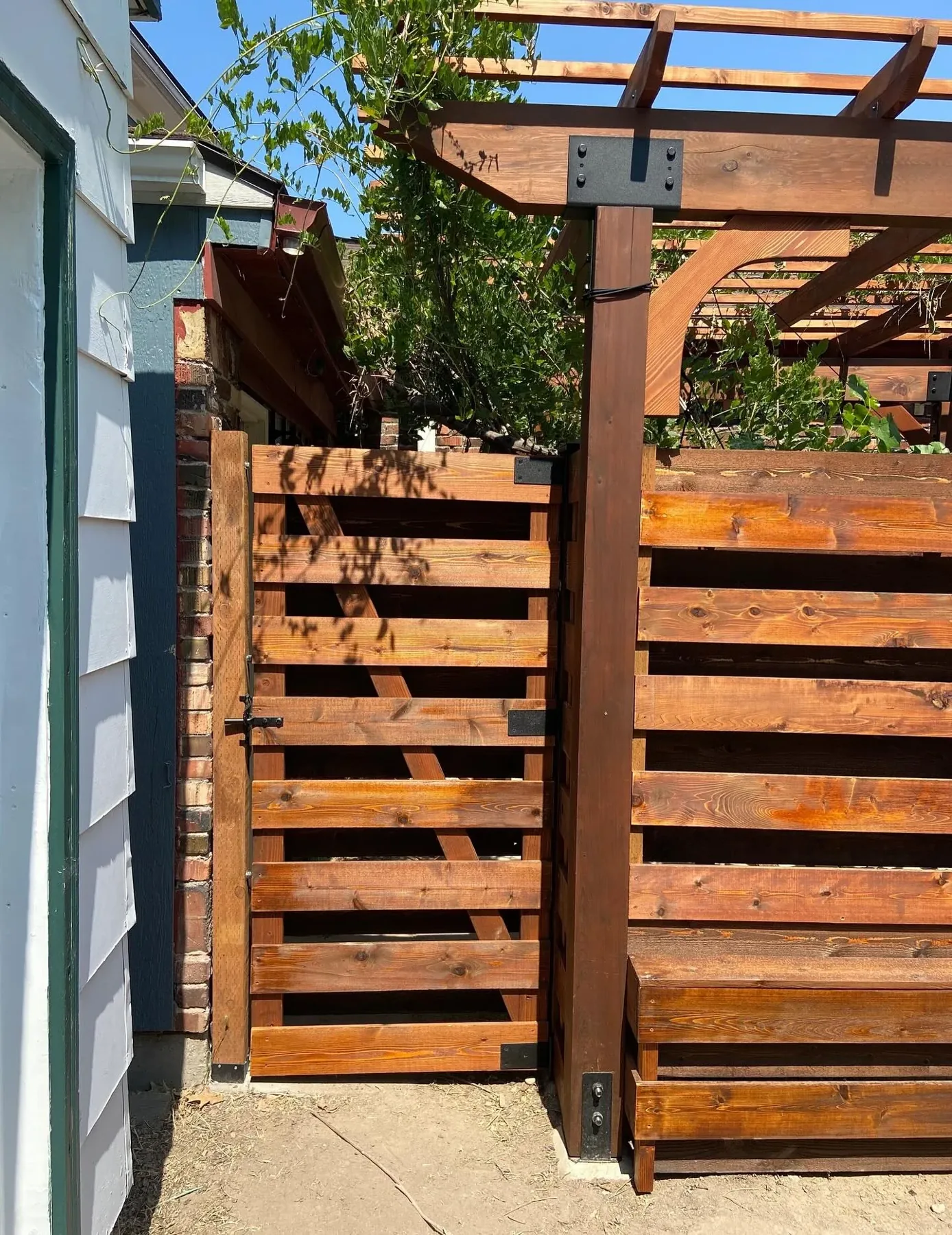 Wood gate below a timber pergola with curved brace and black connection hardware