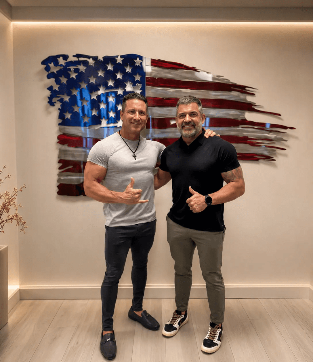 Two men giving thumbs up in front of a wooden American flag
