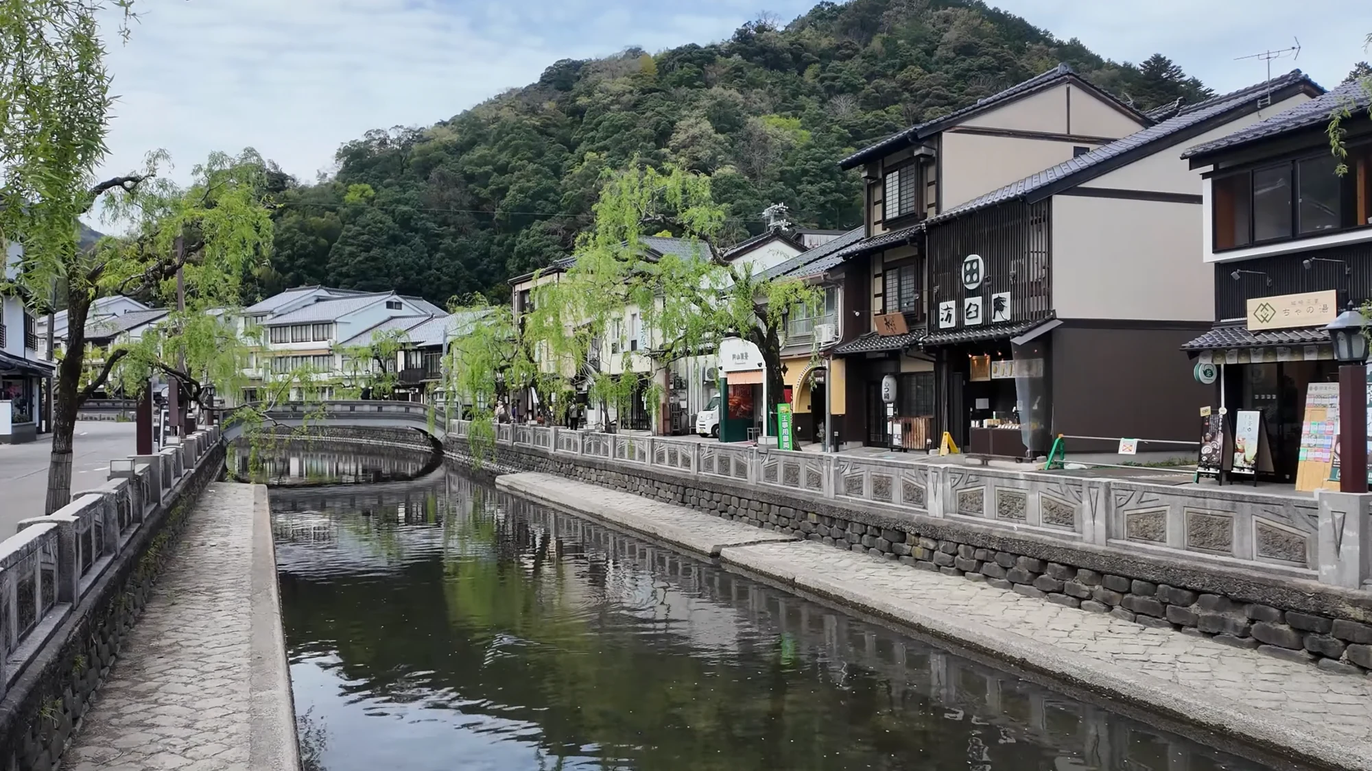 The Otani canal in Kinosaki with fresh willows over stone bridges and inns along both banks.