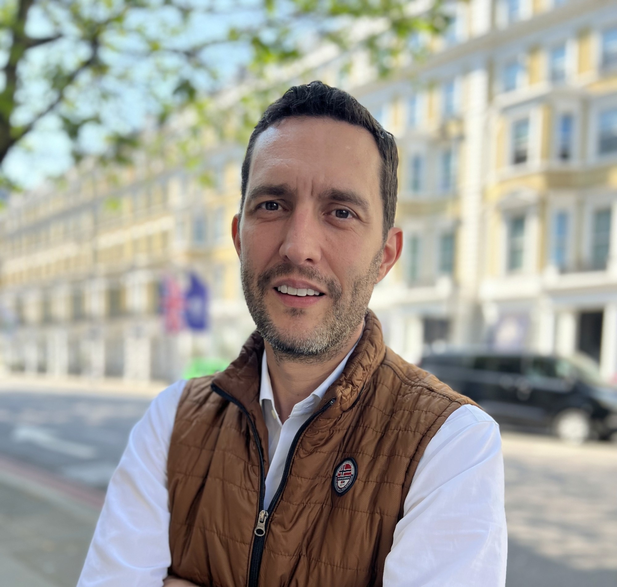 Roberto Taracido Ruiz, Florence's Chief Revenue Officer, wearing a brown vest jacket, standing outdoors on a city street