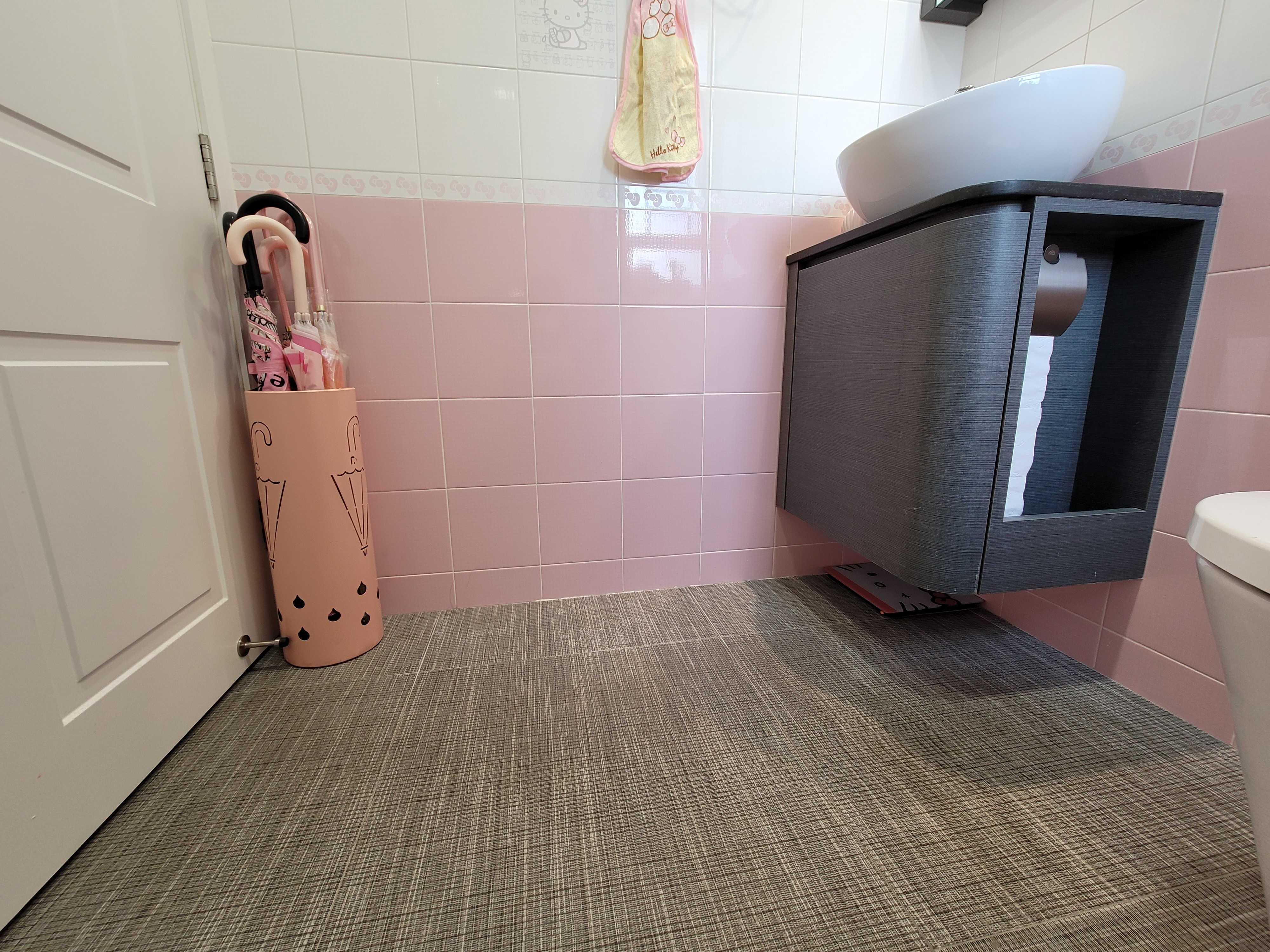 White porcelain vessel sink sits on a charcoal gray textured cabinet against pink square tiles in Hoi Tat Estate bathroom design.