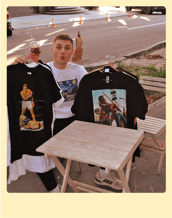 молодиц хлопець тримає у руках чорні футболки з надрукованими малюнками