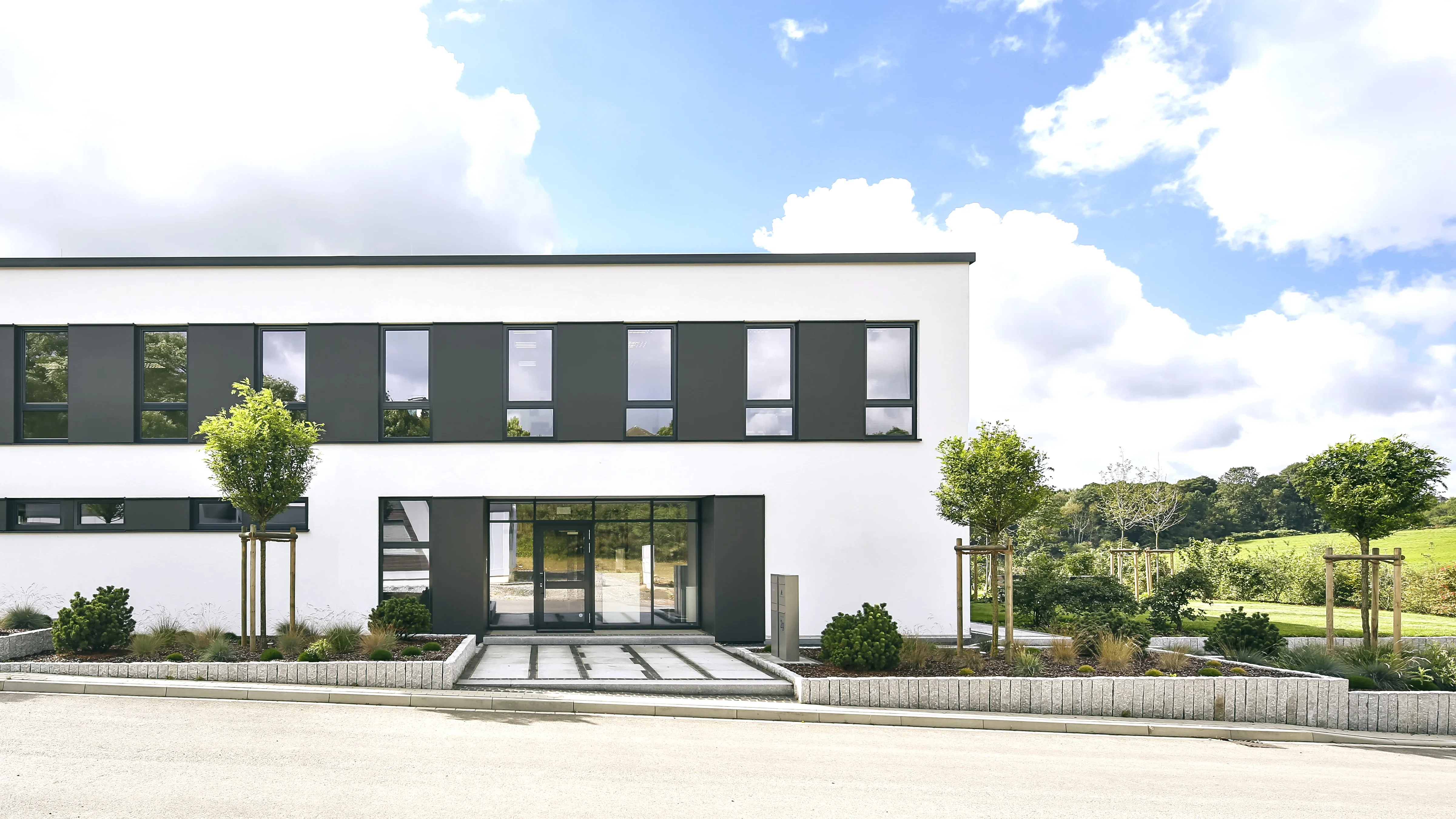 Moderne weiße Bürogebäude mit vielen Fenstern und einer gepflegten Grünanlage davor.