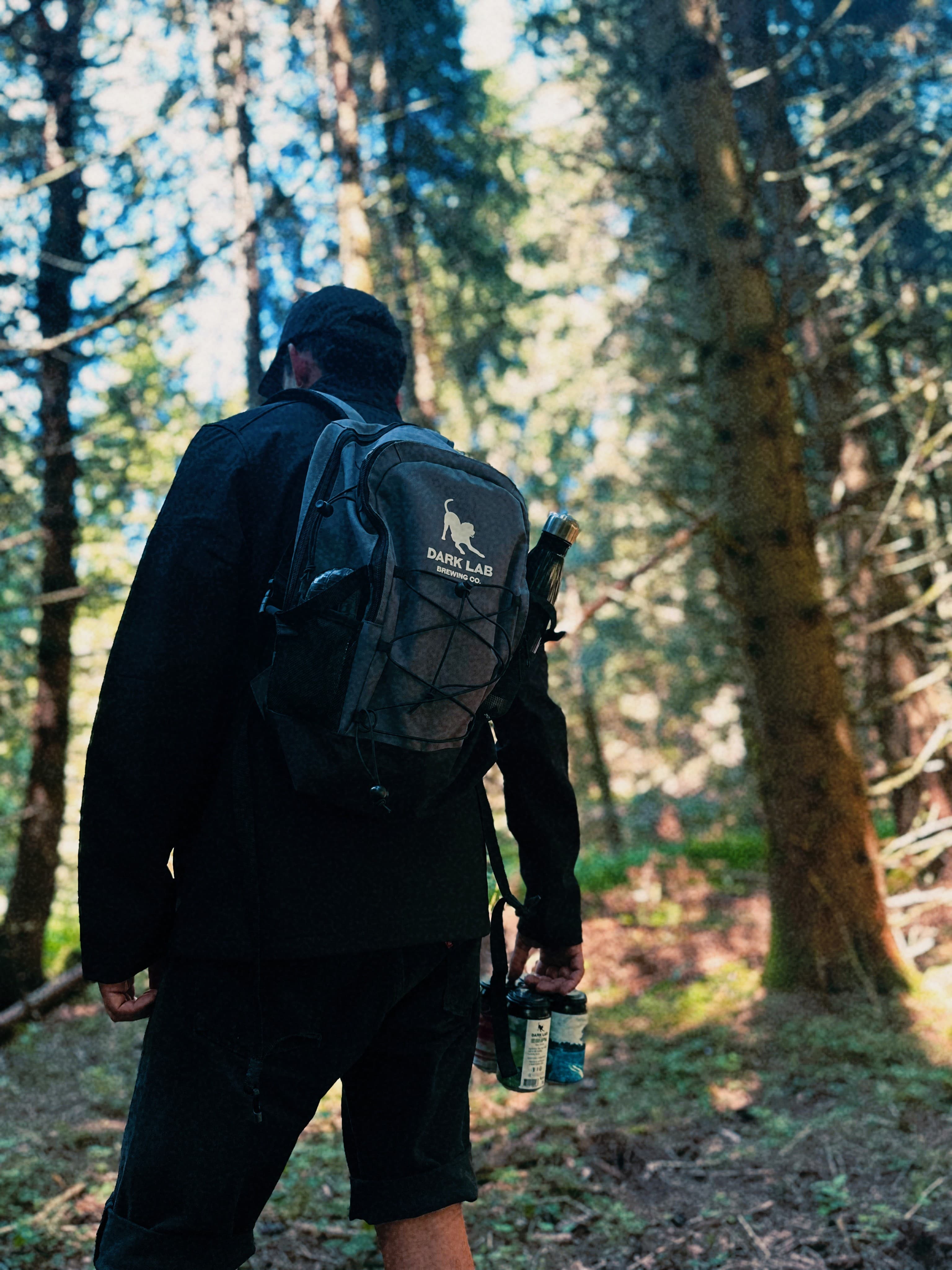 homme de dos avec sac à dos dark lab et pack de 4 canettes à la main