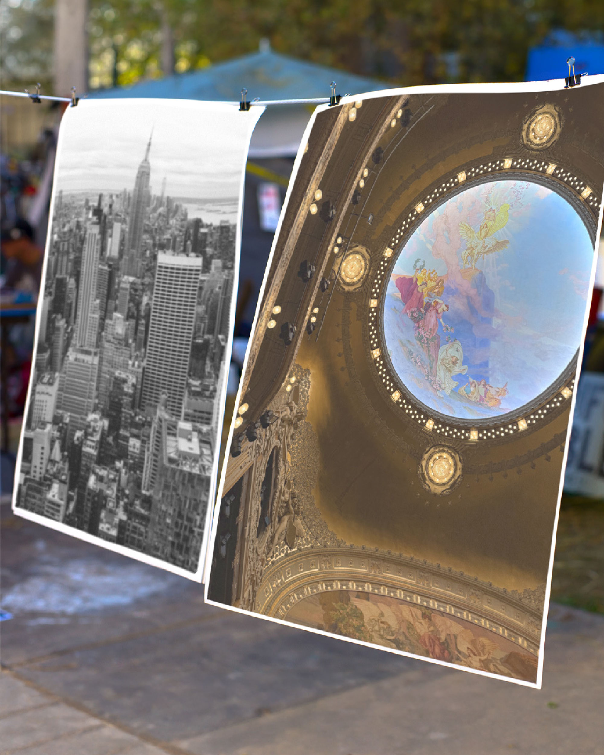 Two photographic prints hanging outdoors, showing a city skyline and an ornate circular ceiling.