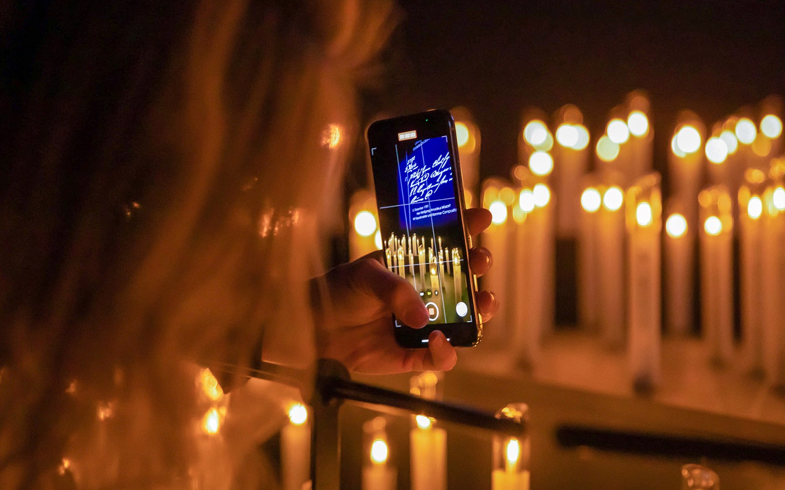 Person photographing candlelit scene with phone at Mythos Mozart event.