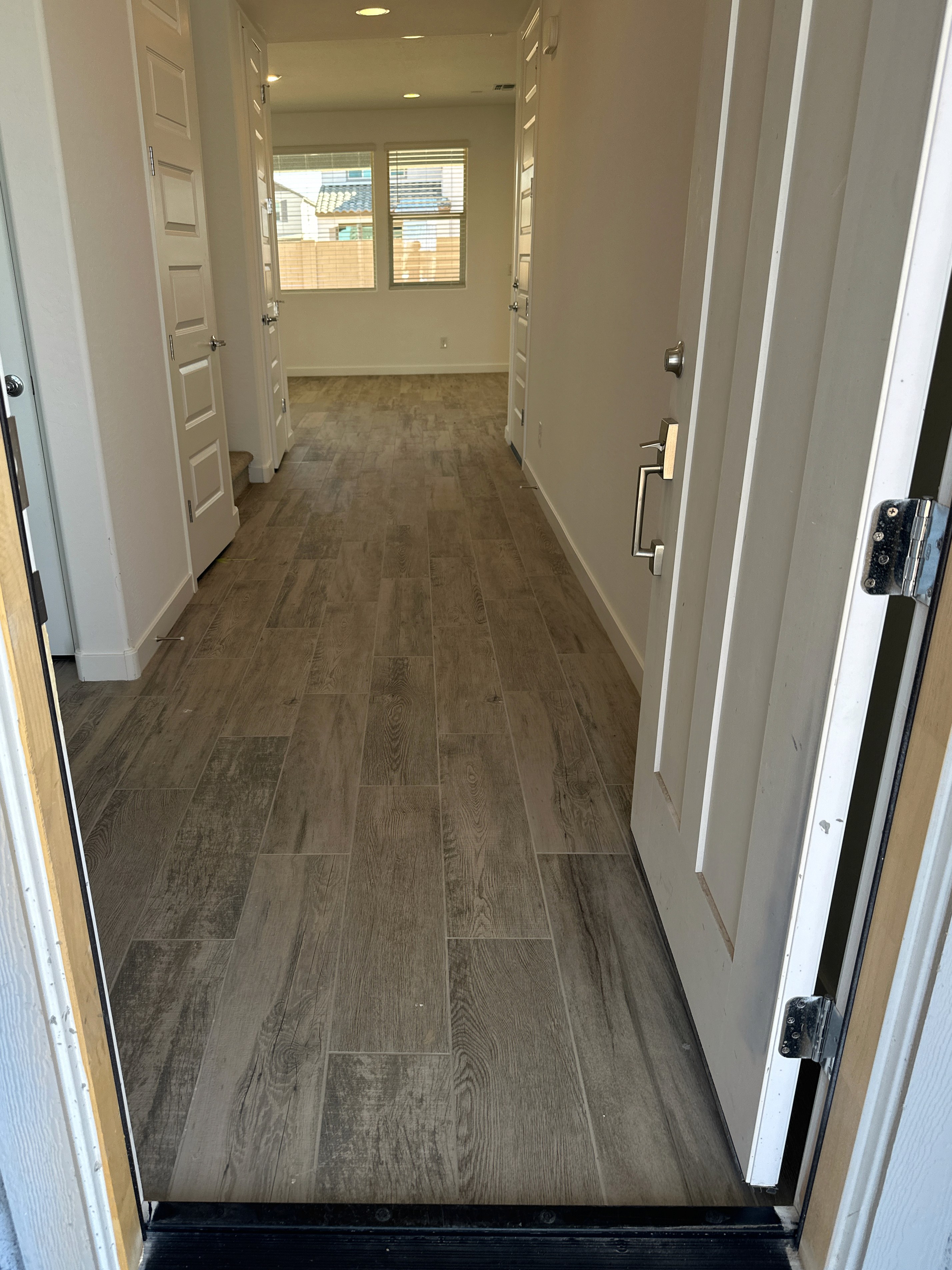 Modern hallway with wood-look tiles, white walls, and doors leading to an open living space during construction.