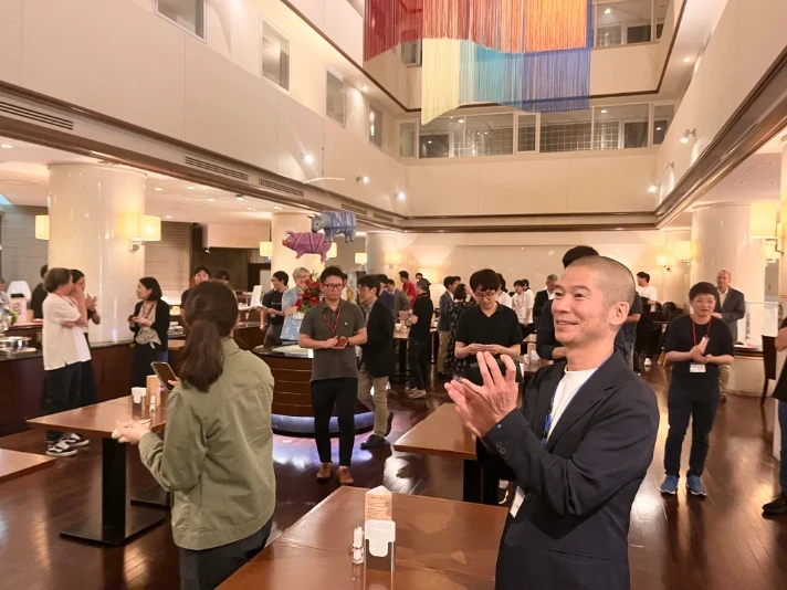 Applause and networking in the atrium; a man in the foreground claps as others socialize in the background.