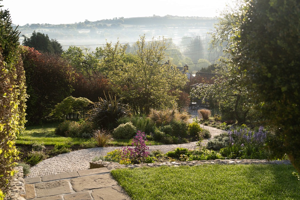 View of the French countryside through a stone villa’s open living room, with sofas and trees framing the scene