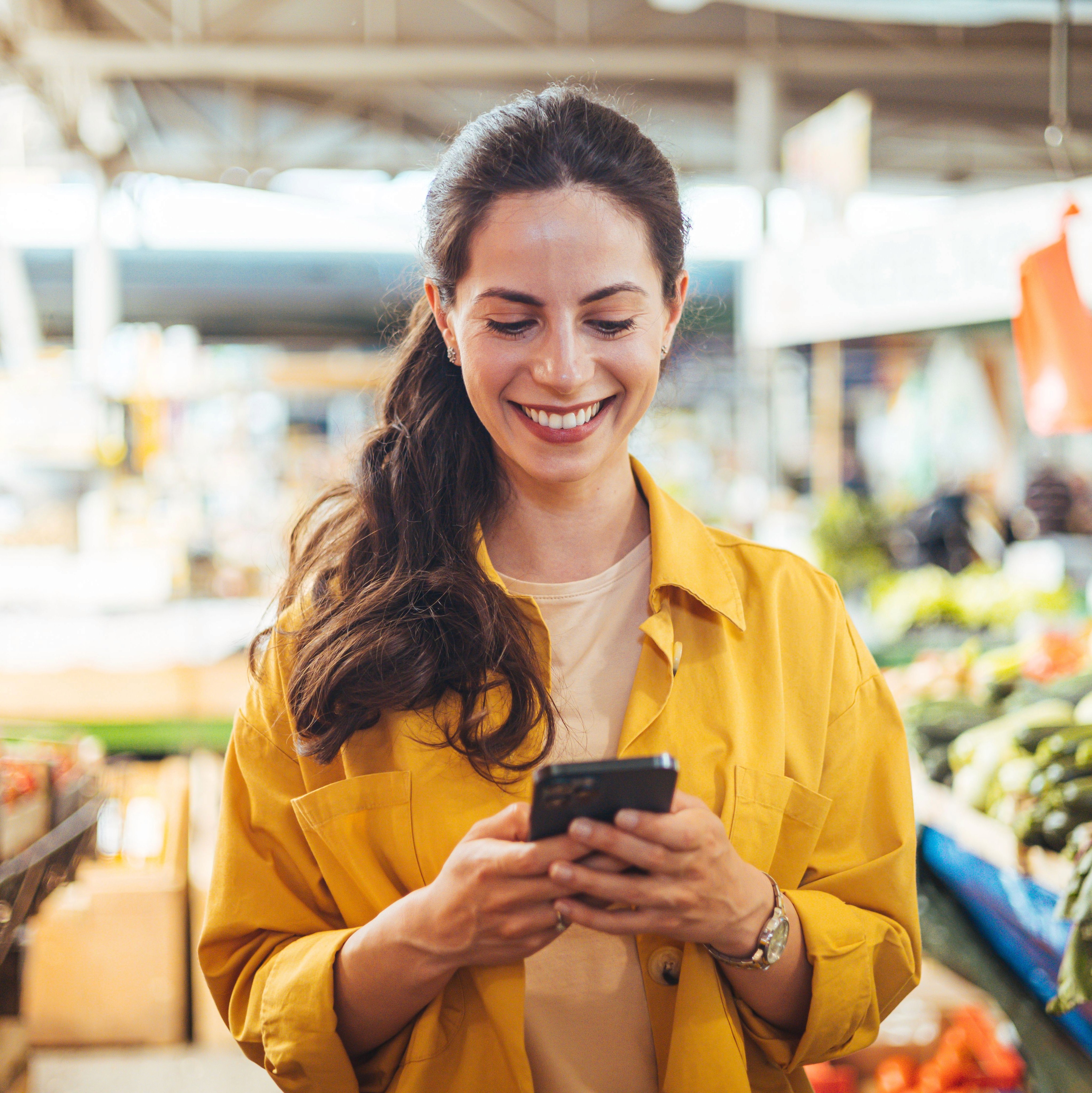 Woman smiling looking at her phone while standing in a supermarket.